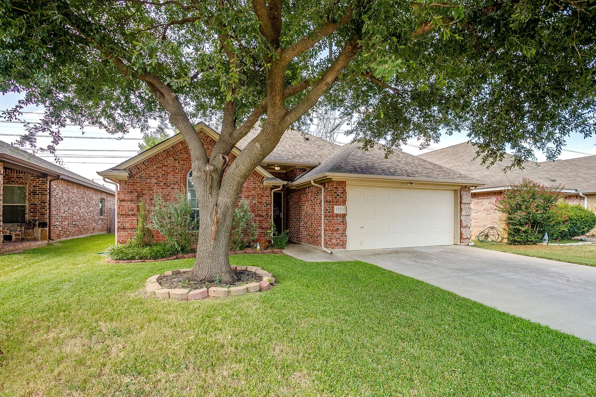 Brick facade residence featuring an attached two-car garage, concrete driveway, and a mature shade tree