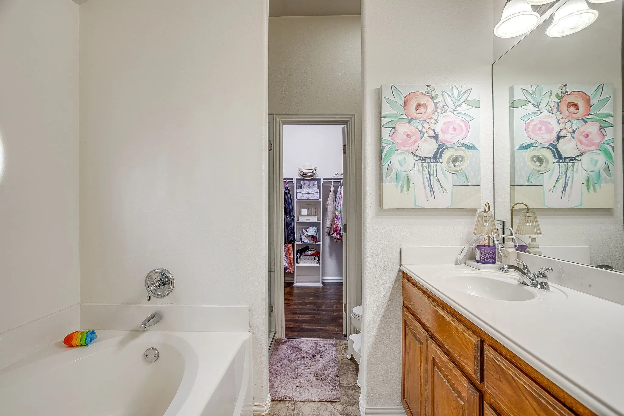 Bathroom featuring a built-in tub with chrome fixtures, a wood vanity with a white countertop and integrated sink, a large wall-mounted mirror, and overhead vanity lighting