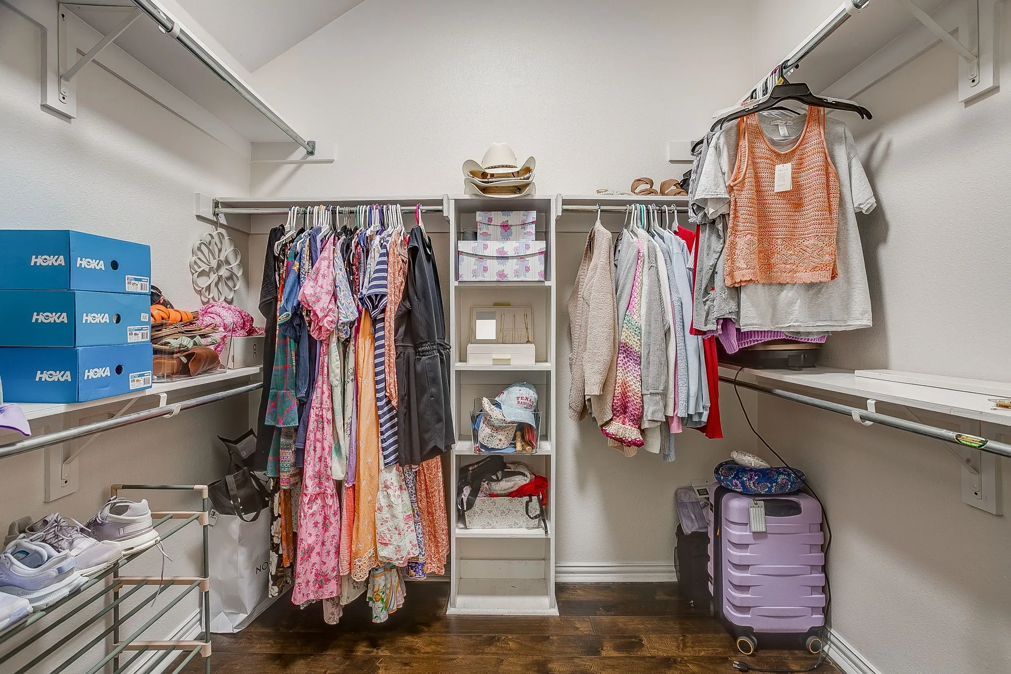 Walk-in closet featuring built-in shelving, multiple hanging rods, corner shelving unit, and wood-finish flooring