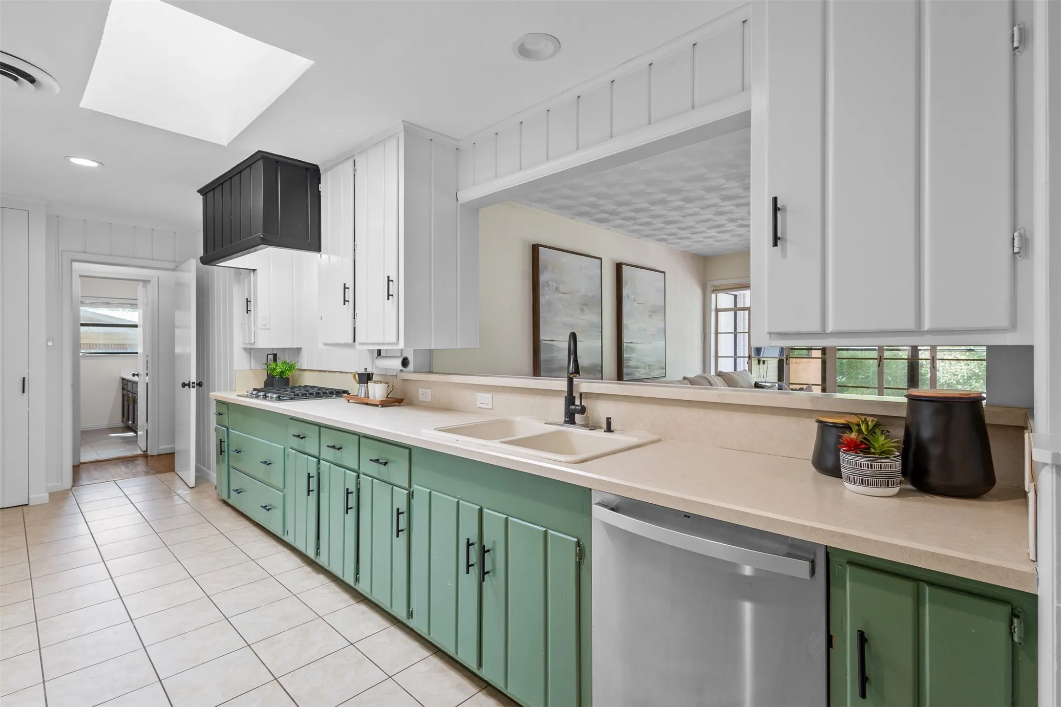 Kitchen featuring dual-toned cabinetry, light-toned countertops, tile flooring, and a skylight