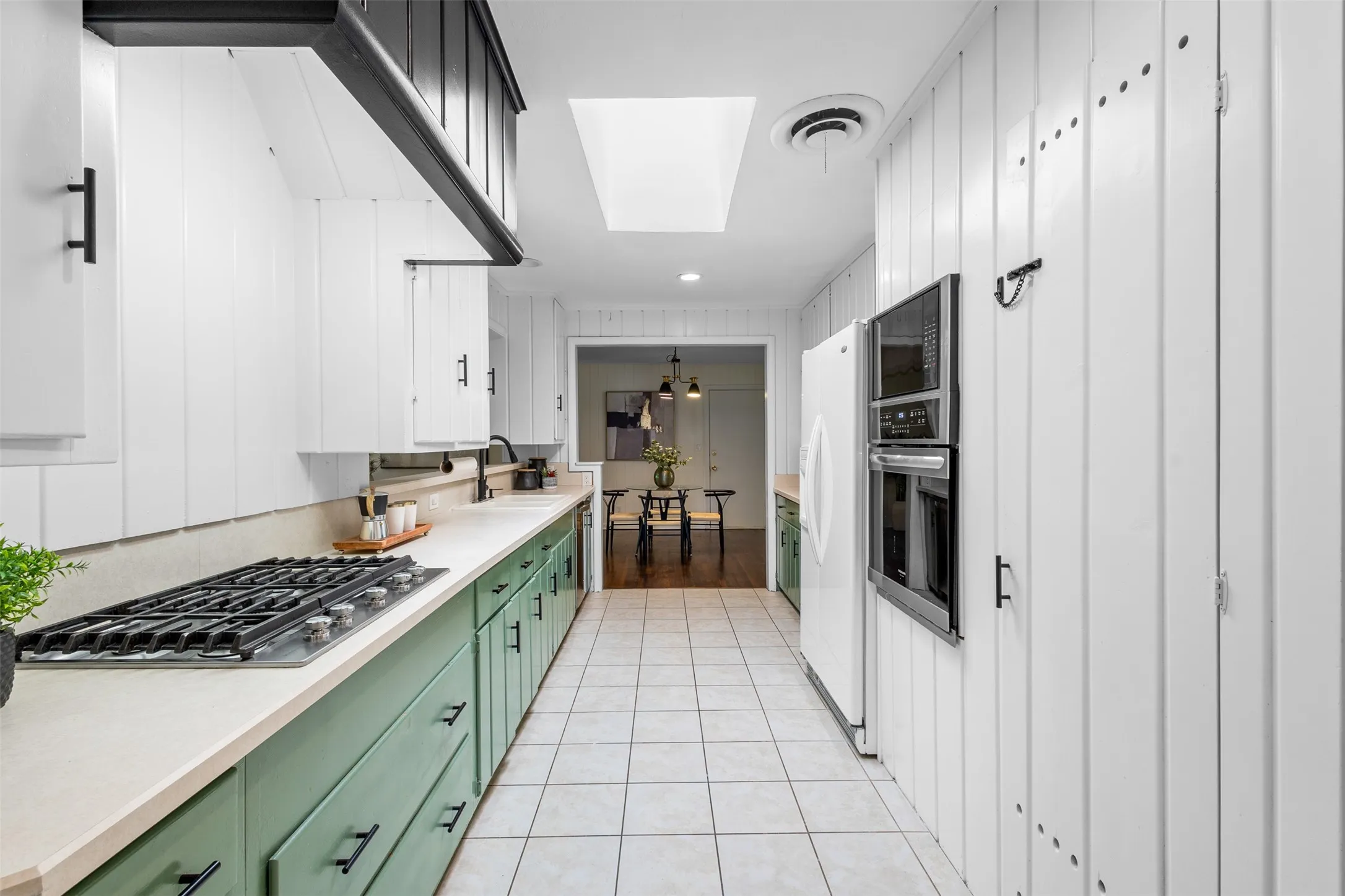 Galley kitchen featuring a gas range, built-in wall oven, white cabinetry with black hardware, and light-colored countertops