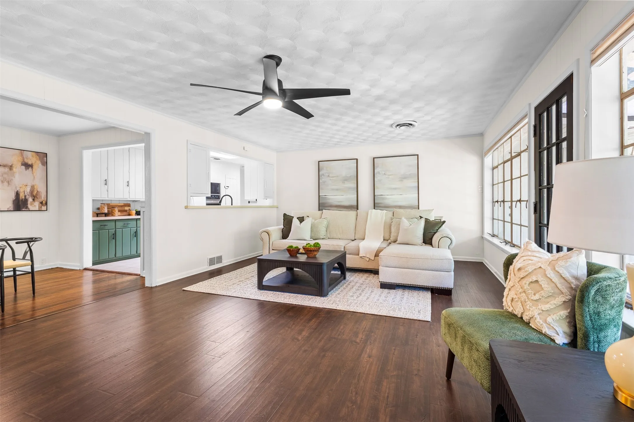 Living area featuring rich wood-finish flooring, a modern ceiling fan with lighting, and extensive multi-pane windows