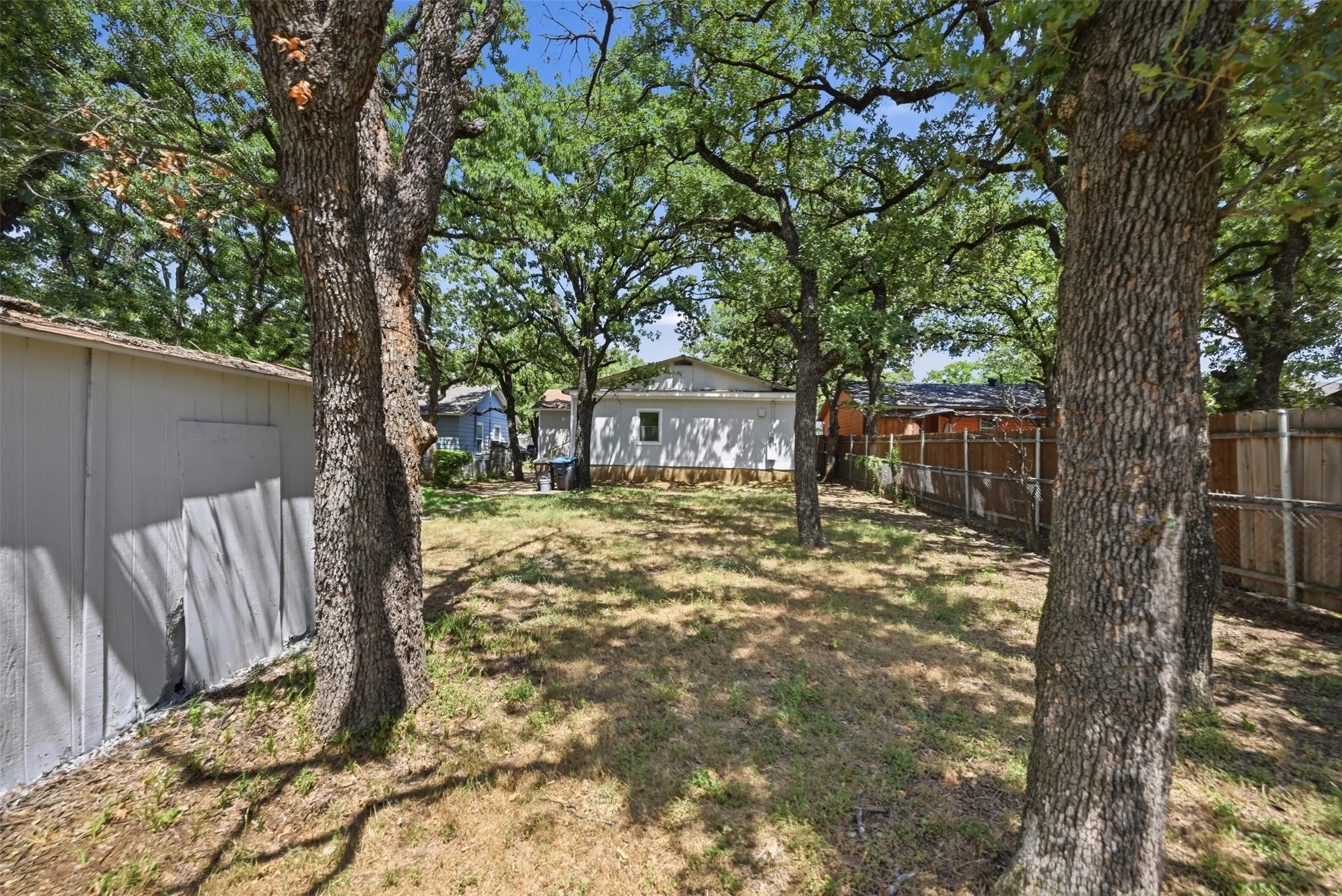 Spacious backyard featuring multiple mature trees, a wooden privacy fence, and a storage shed