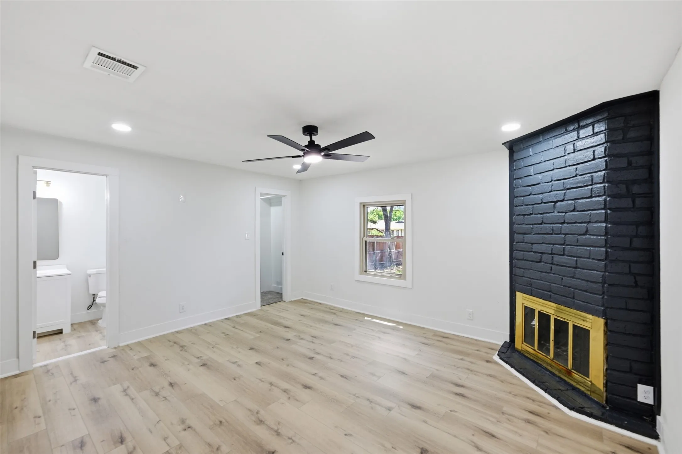 Spacious room featuring wood-finish flooring, a black brick fireplace with a brass-toned insert, a ceiling fan with integrated lighting, and recessed ceiling lights