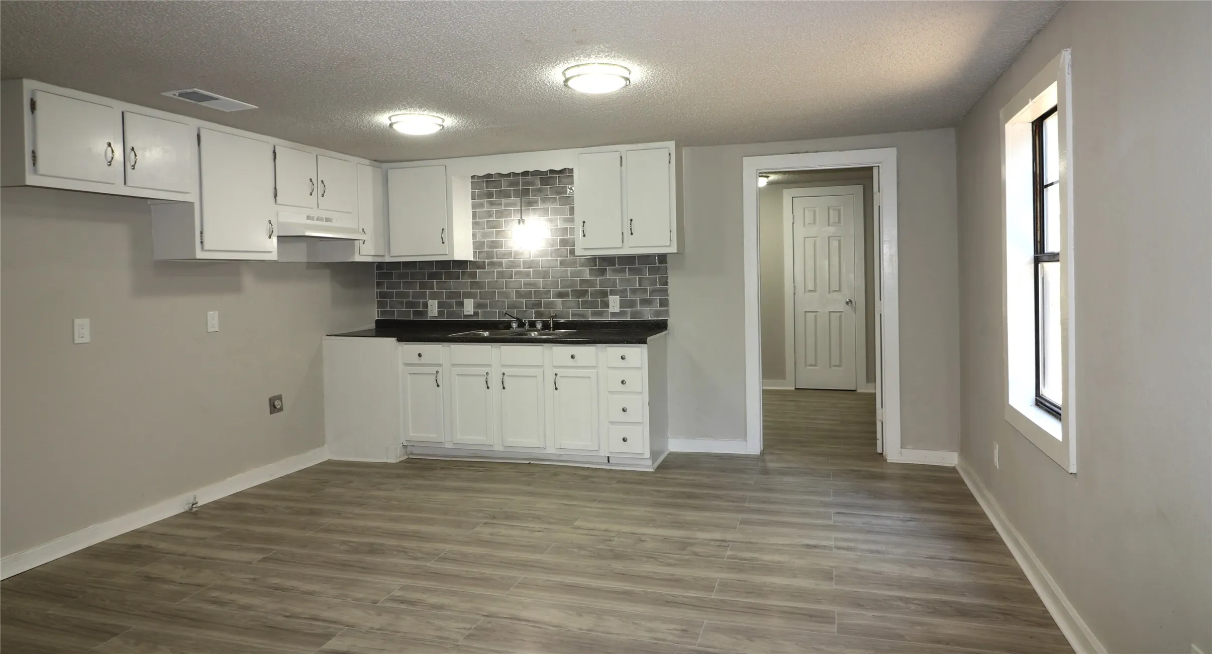 Kitchen with dark countertops, backsplash, white cabinets, dark wood-style floors, and a textured ceiling