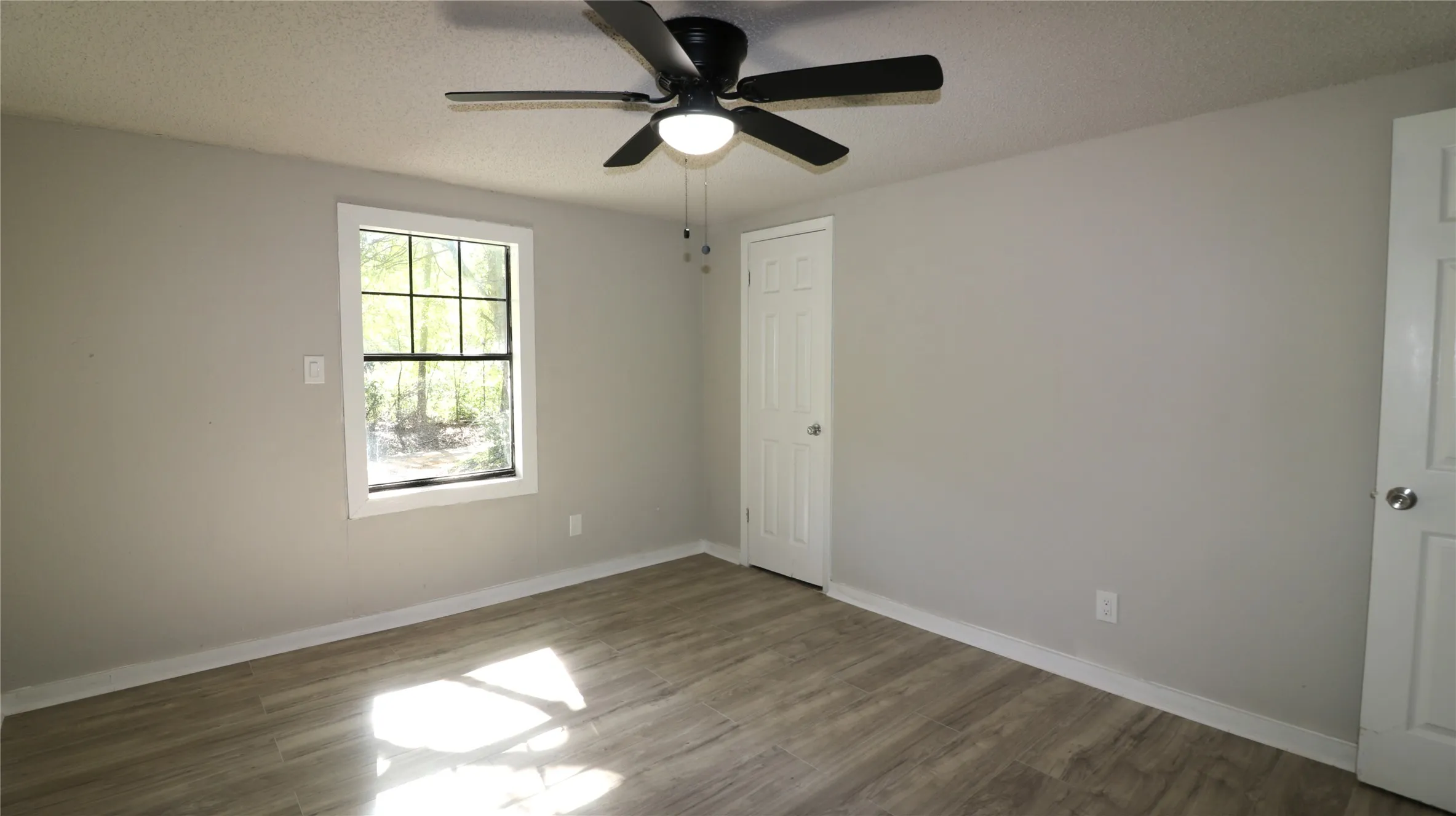 Empty room with a textured ceiling, wood finished floors, and ceiling fan