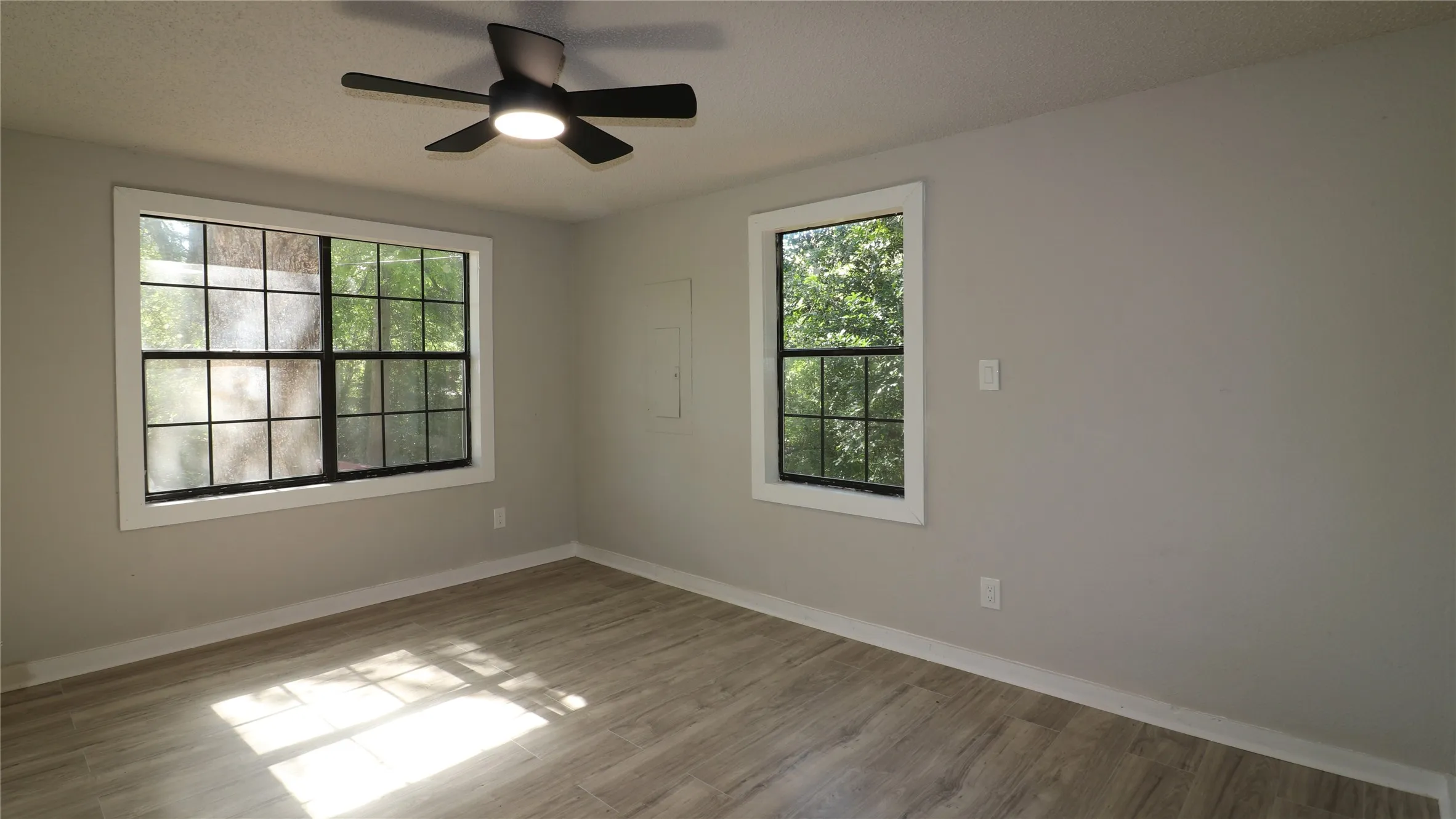 Empty room with light wood finished floors, a ceiling fan, and electric panel