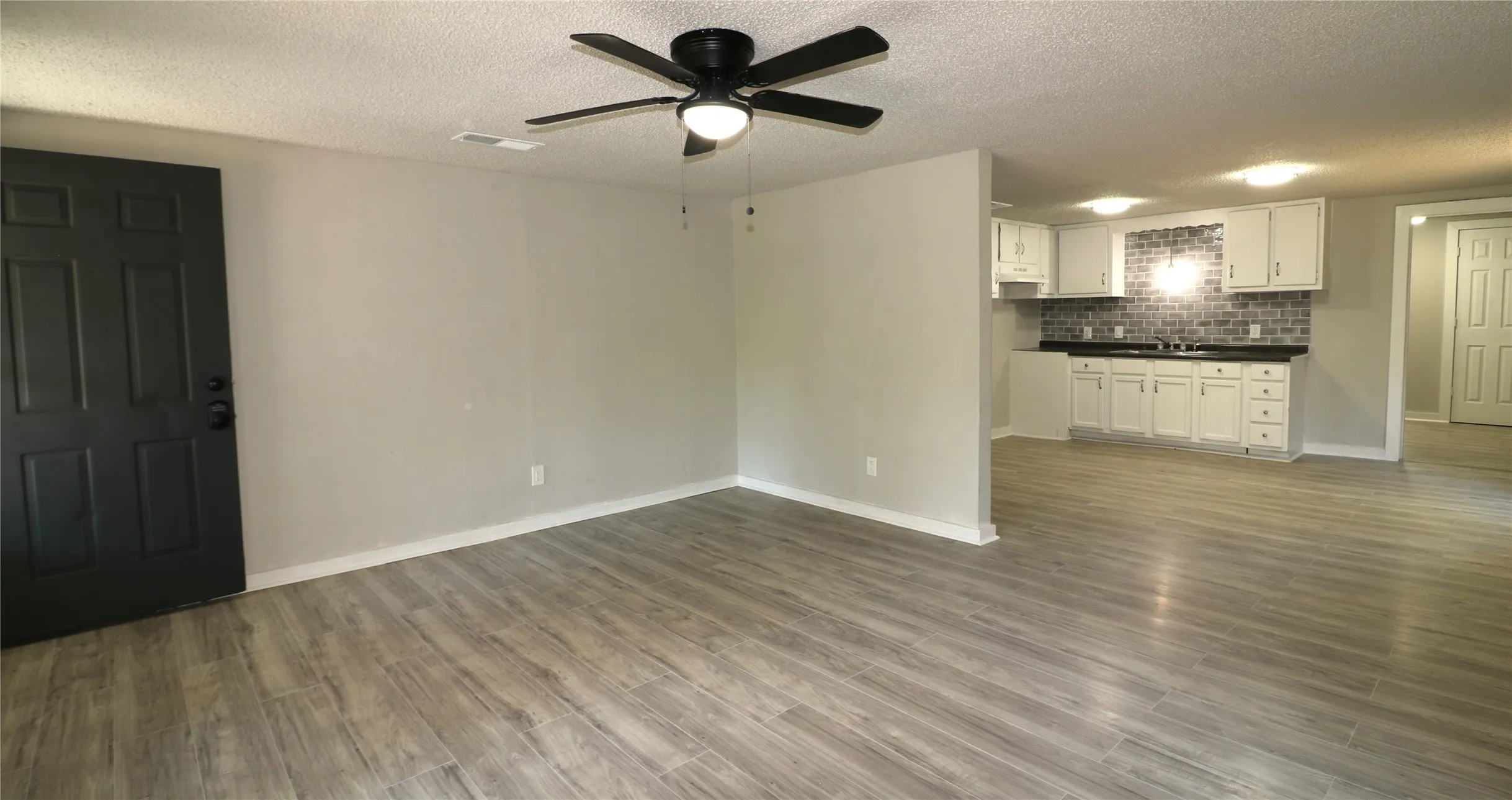 Unfurnished living room featuring a textured ceiling, dark wood-style floors, and a ceiling fan