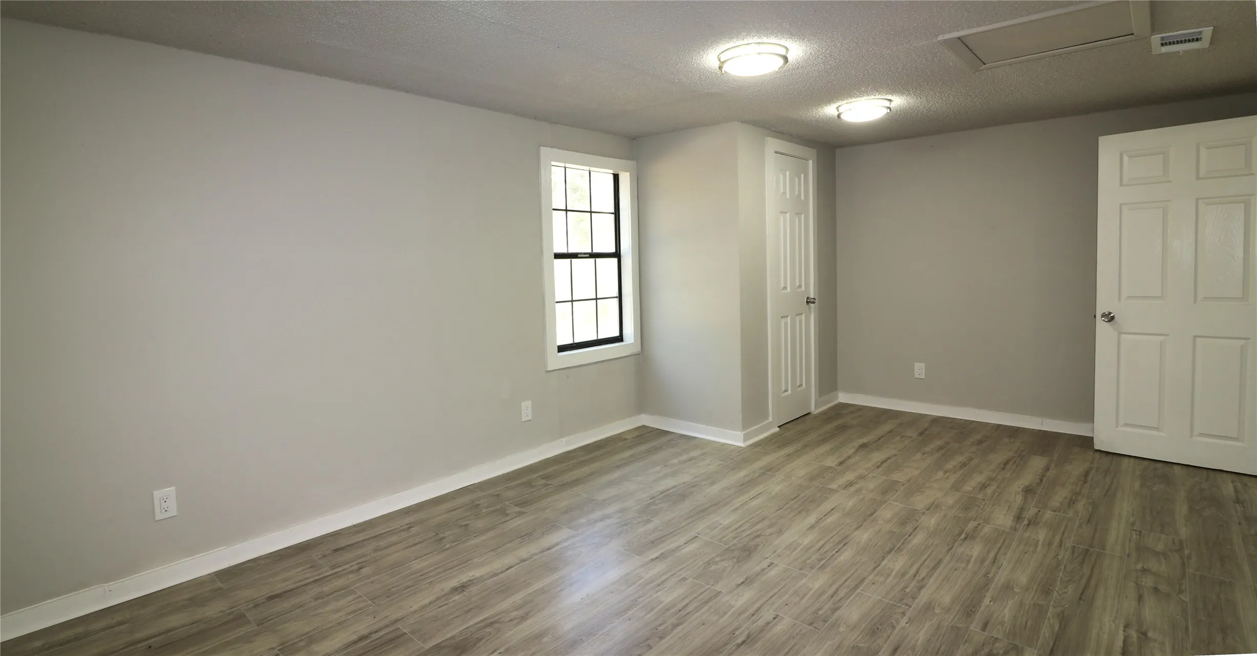 Unfurnished bedroom with a textured ceiling, wood finished floors, and attic access