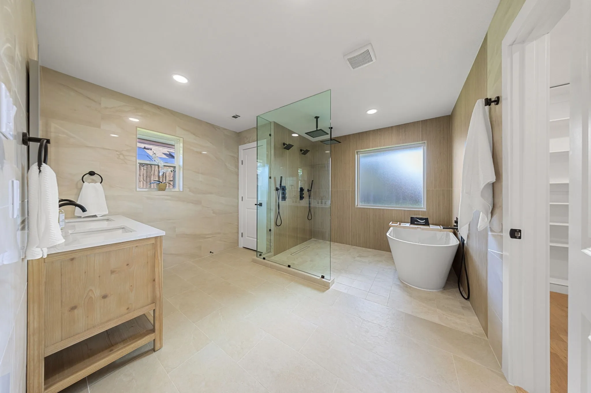 Spacious bathroom featuring a frameless glass shower enclosure, freestanding soaking tub, wood-finish vanity with countertop, and recessed lighting