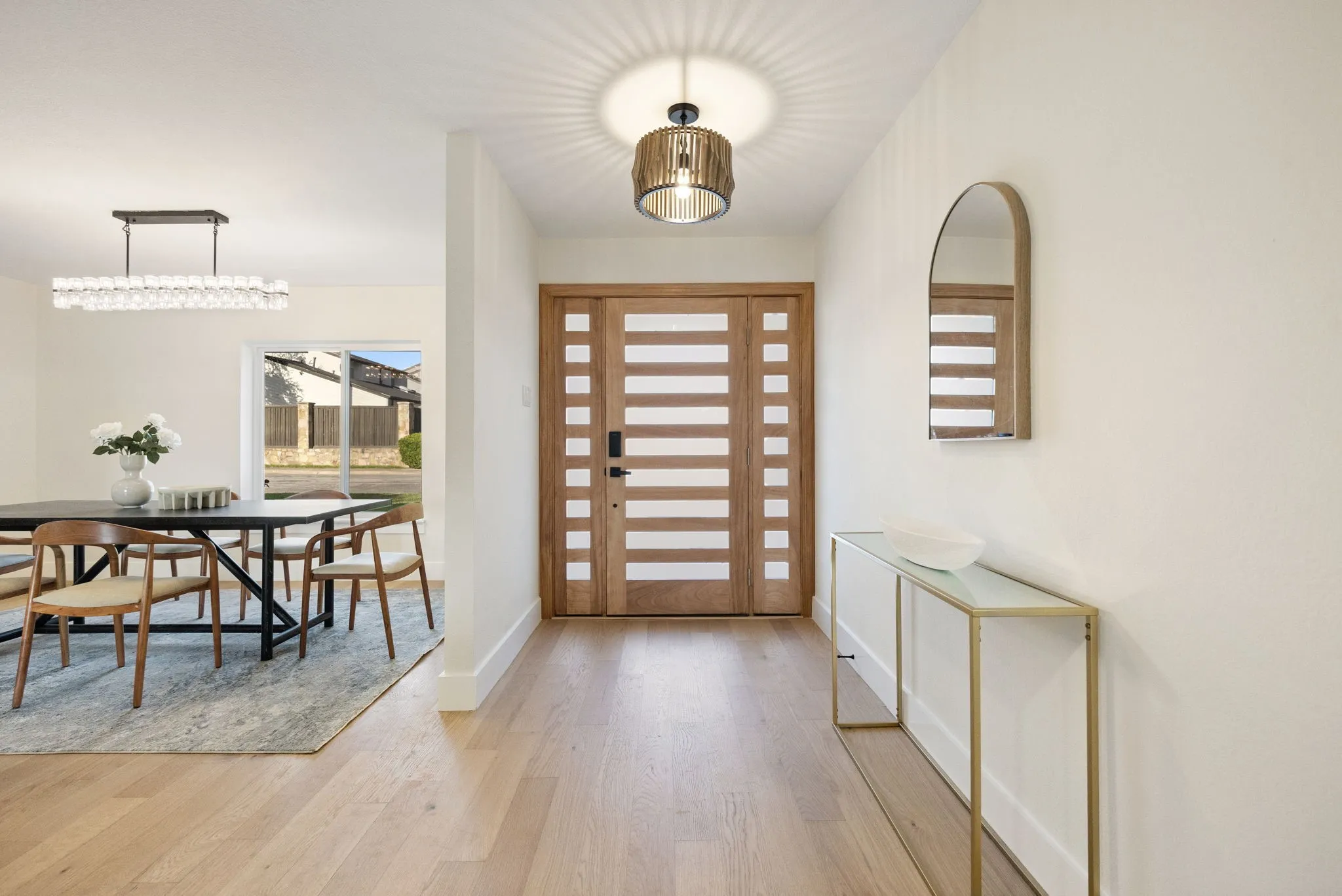 Light wood-finish flooring extends from the entryway, featuring a modern wood entry door with horizontal frosted glass panes