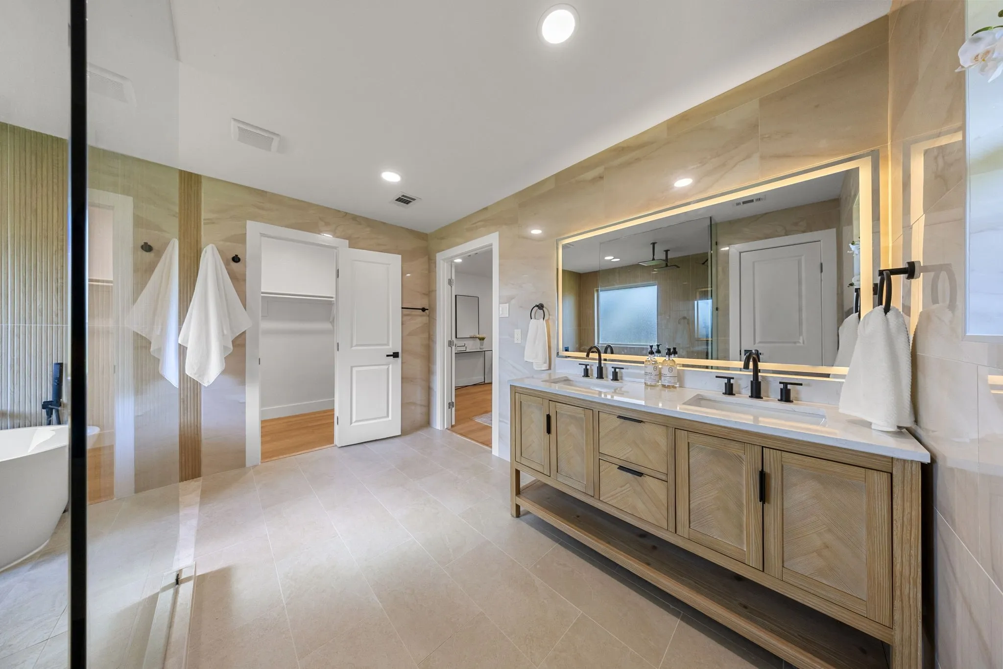 Spacious bathroom featuring a dual vanity with light-wood finish cabinetry and a white countertop