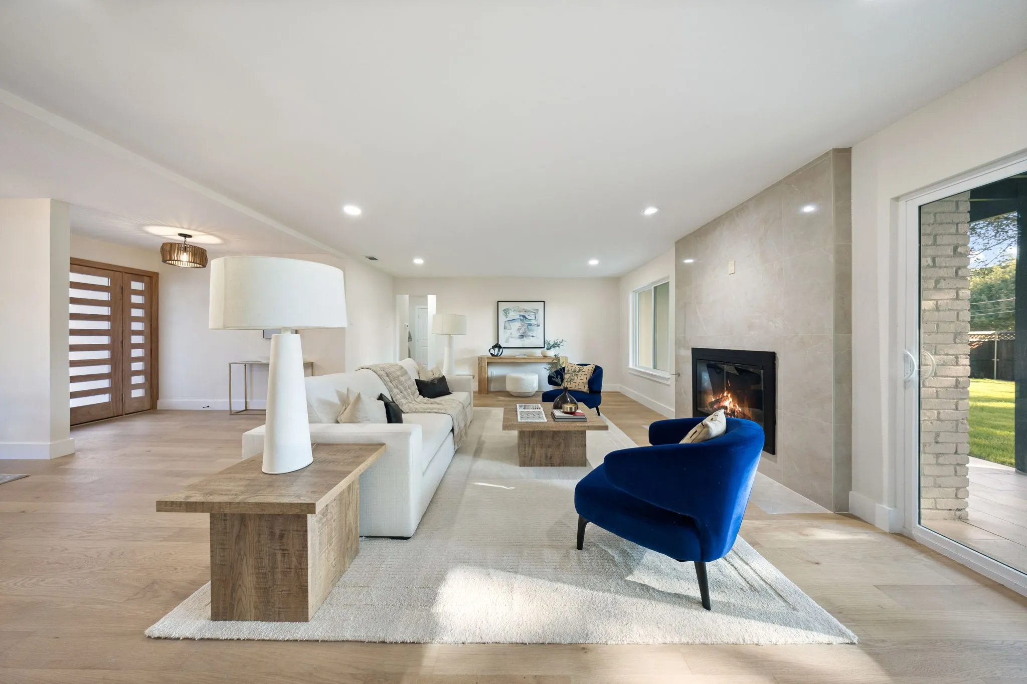Spacious living area featuring light wood-finish flooring and a contemporary fireplace with a light-toned stone surround