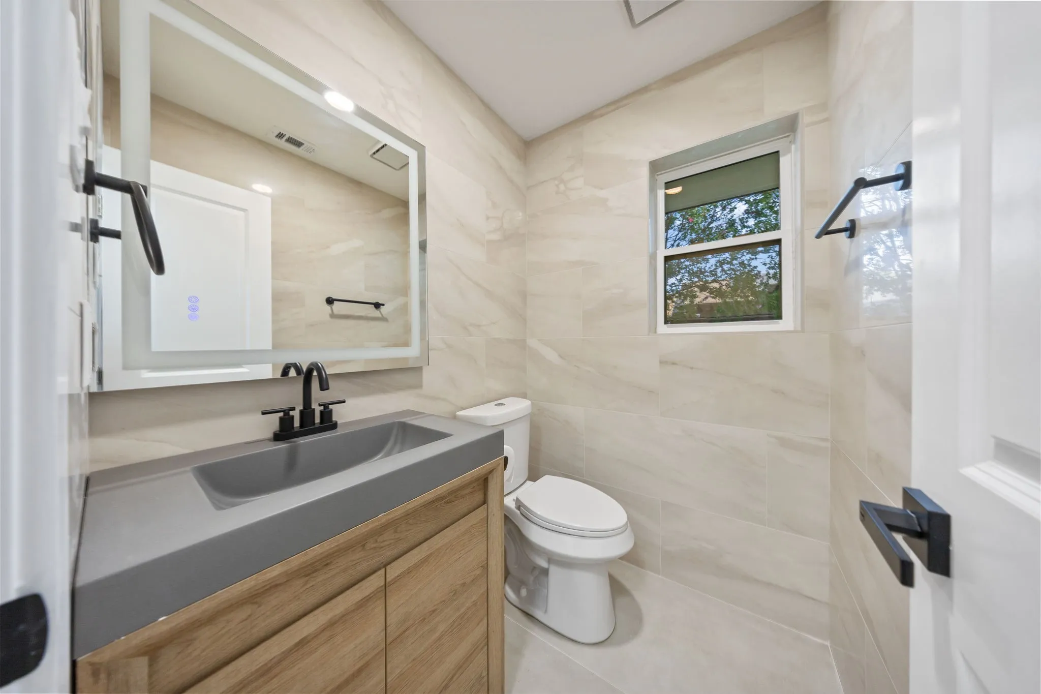 Powder bathroom featuring a wood-finish vanity with an integrated gray sink basin and matte black fixtures