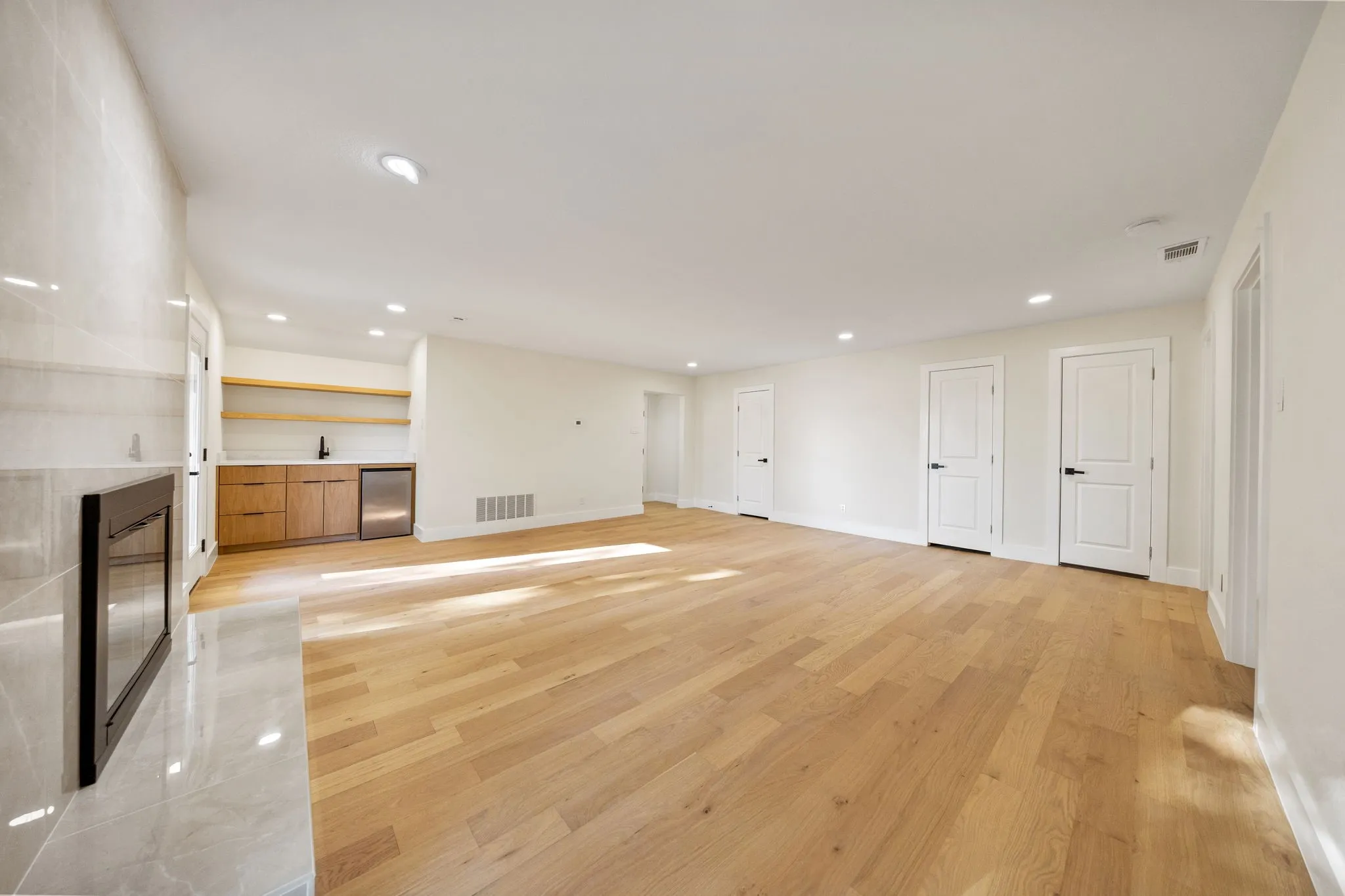 Spacious room featuring wood-finish flooring, recessed lighting, and a modern fireplace with a tiled surround