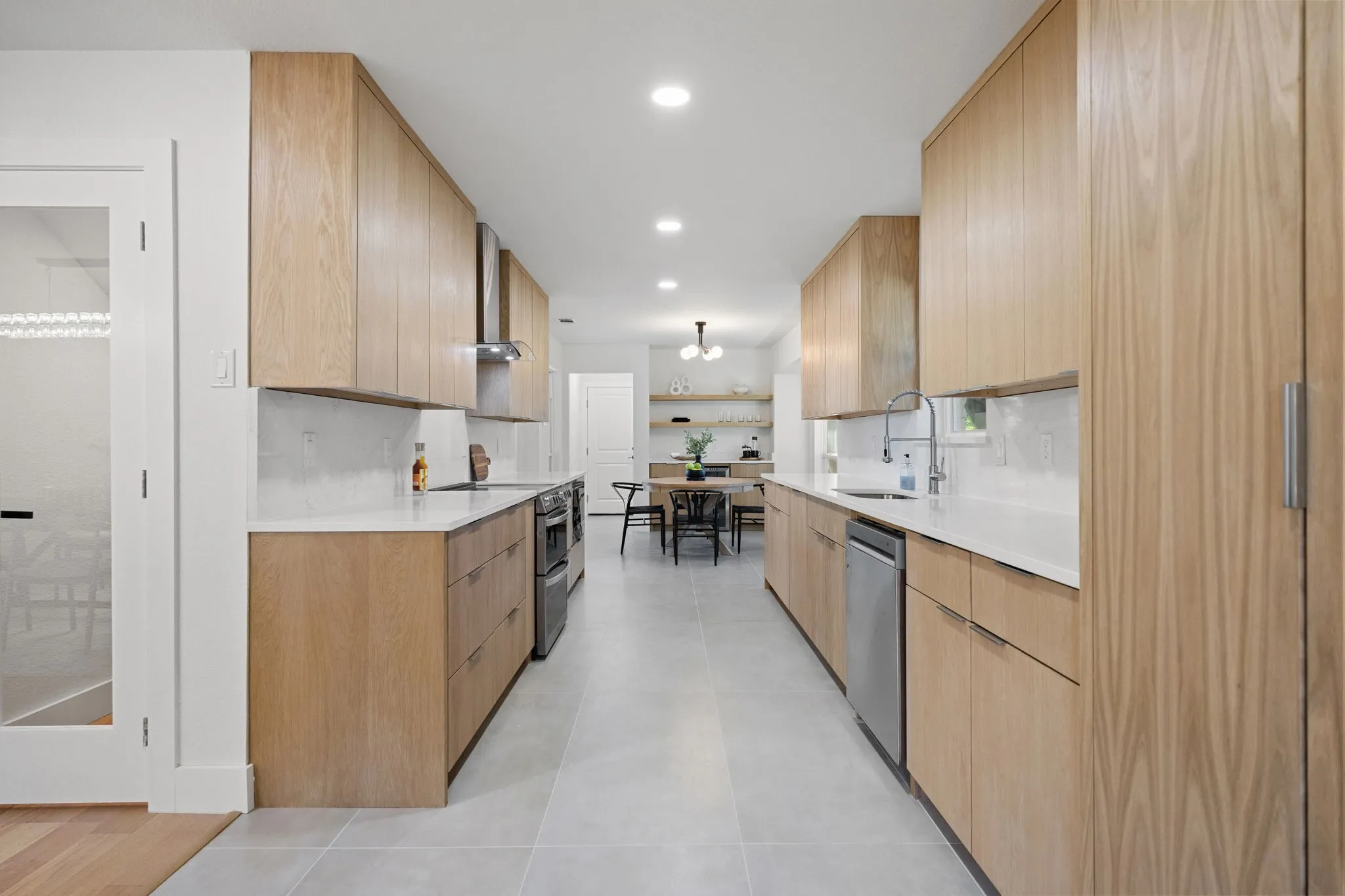 Galley kitchen featuring light wood-finish cabinetry, stainless steel appliances, white countertops, and a full-height backsplash