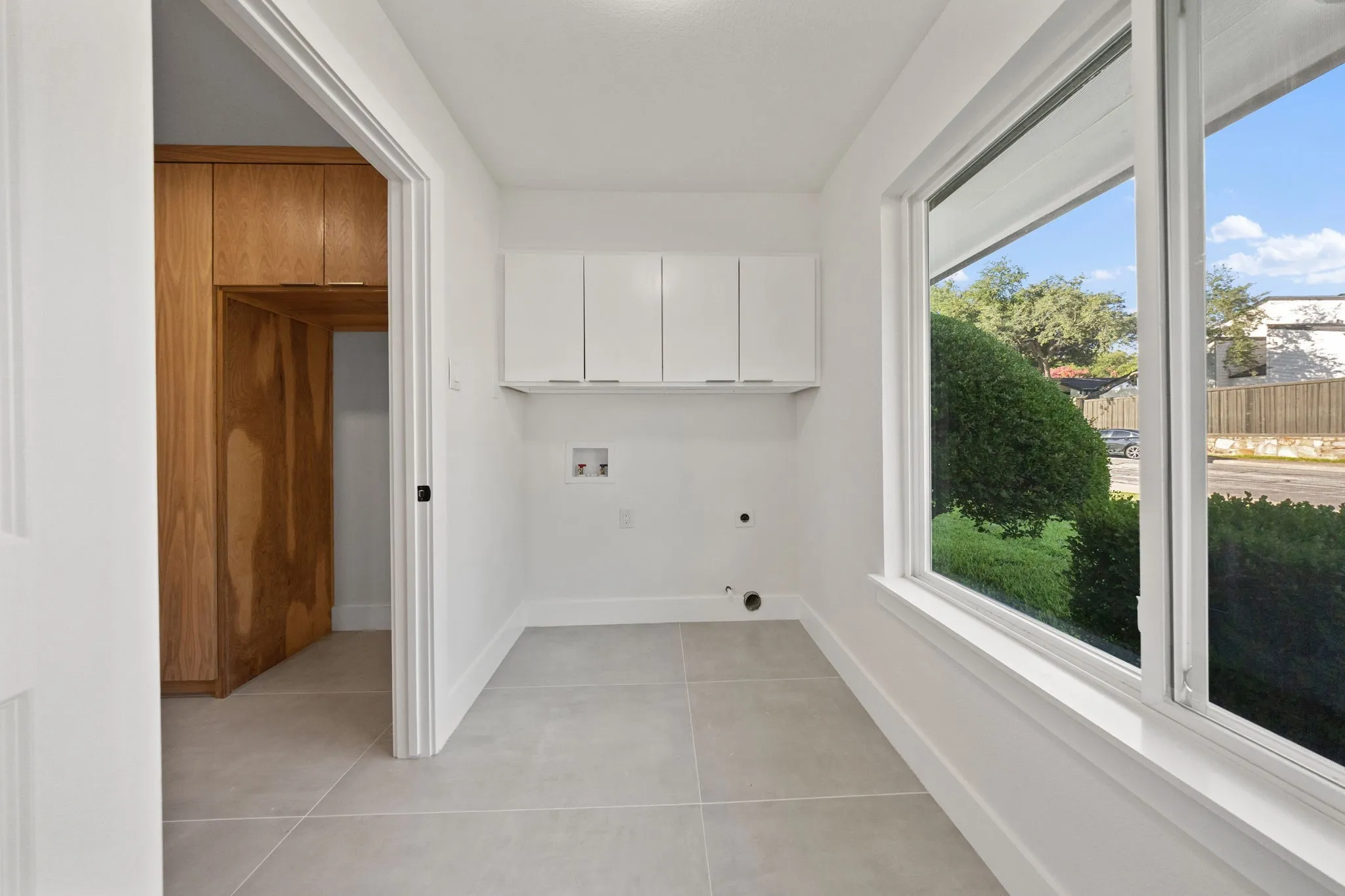 Bright utility space featuring white upper cabinetry, large windows, light tile flooring, and a natural wood-finish built-in storage unit