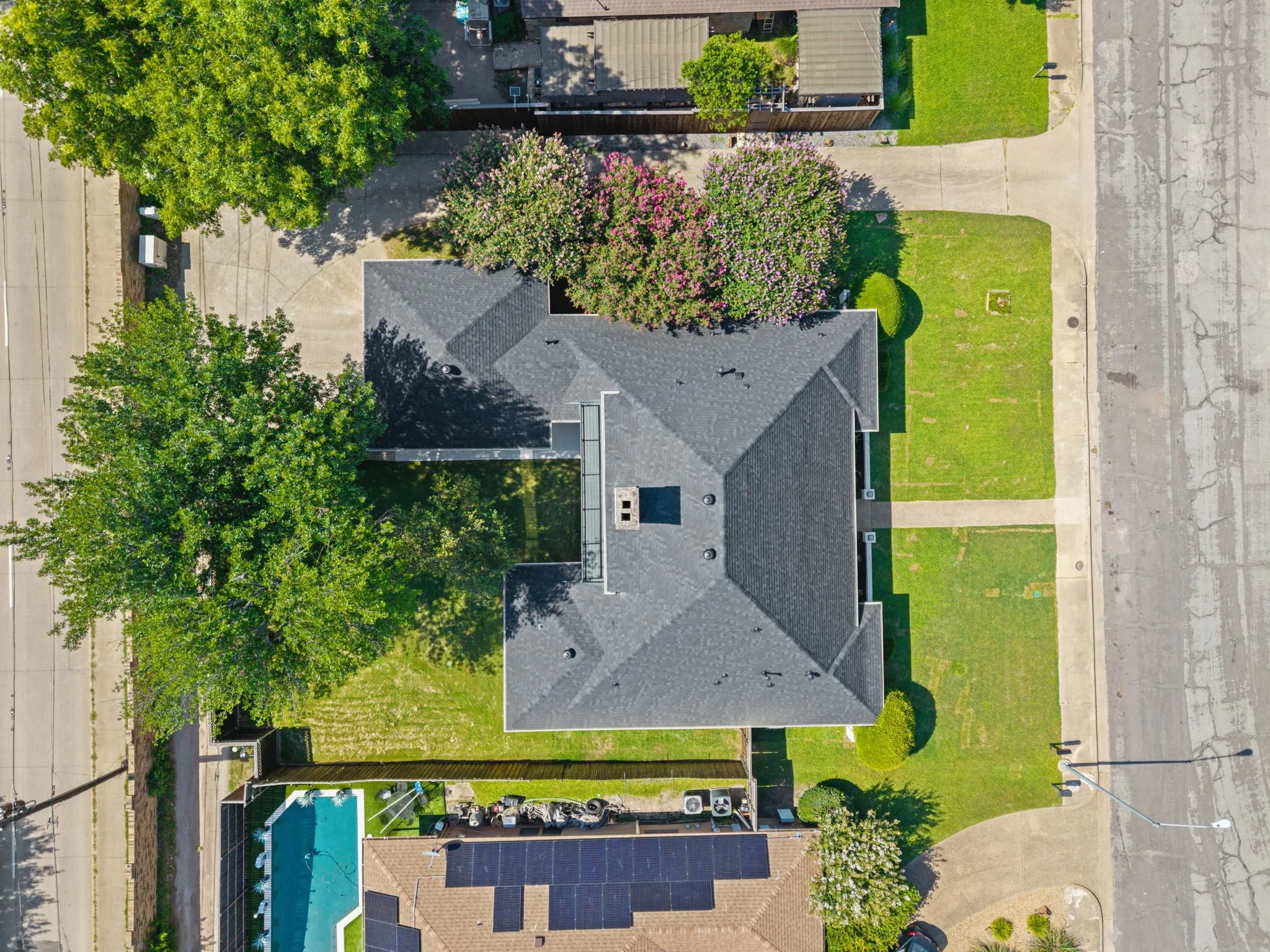 Multi-gabled dark shingle roofline on a property featuring a manicured lawn and mature trees