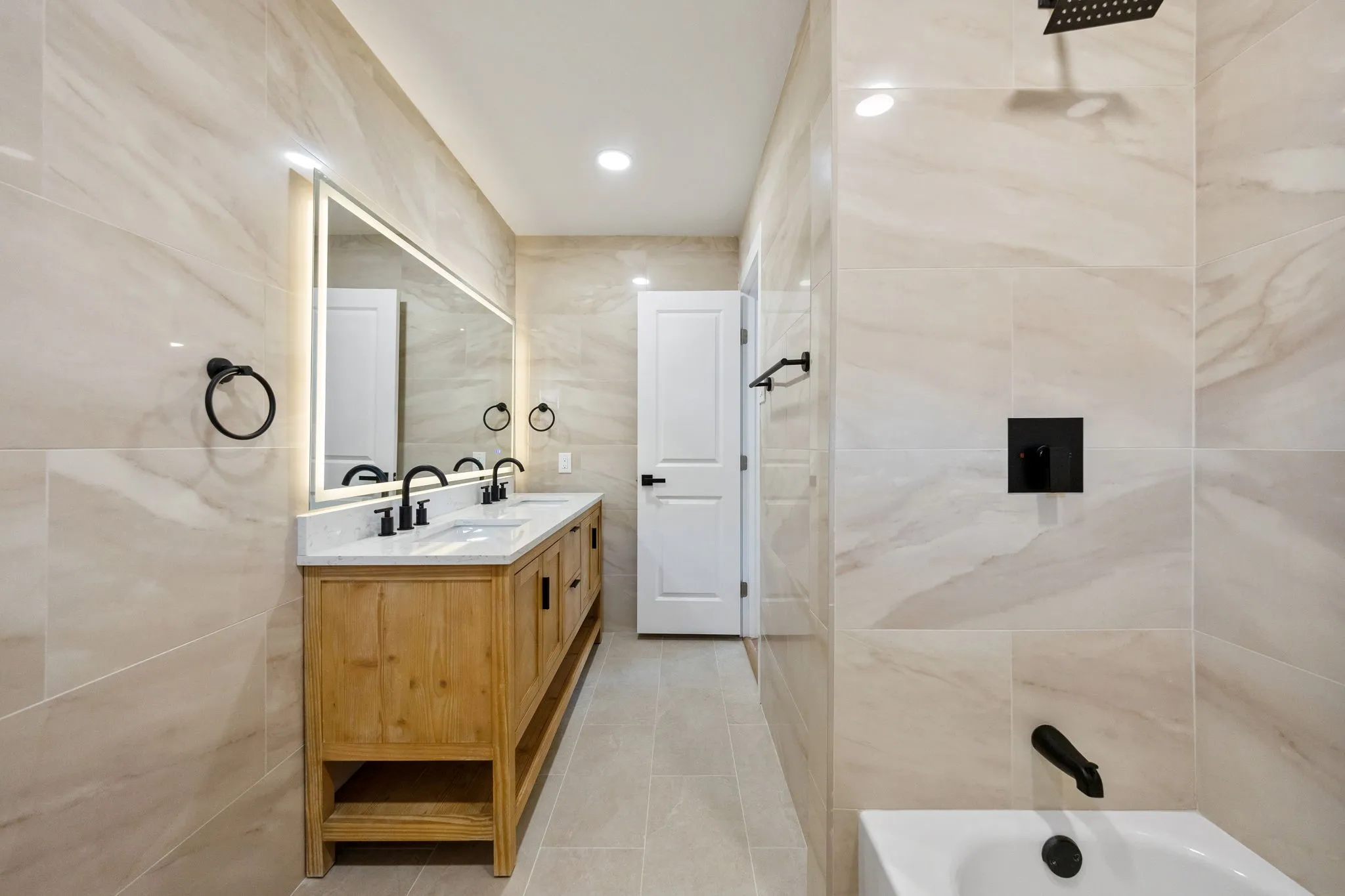 Bathroom featuring a double vanity with a wood-finish cabinet, dual undermount sinks, and a large illuminated mirror