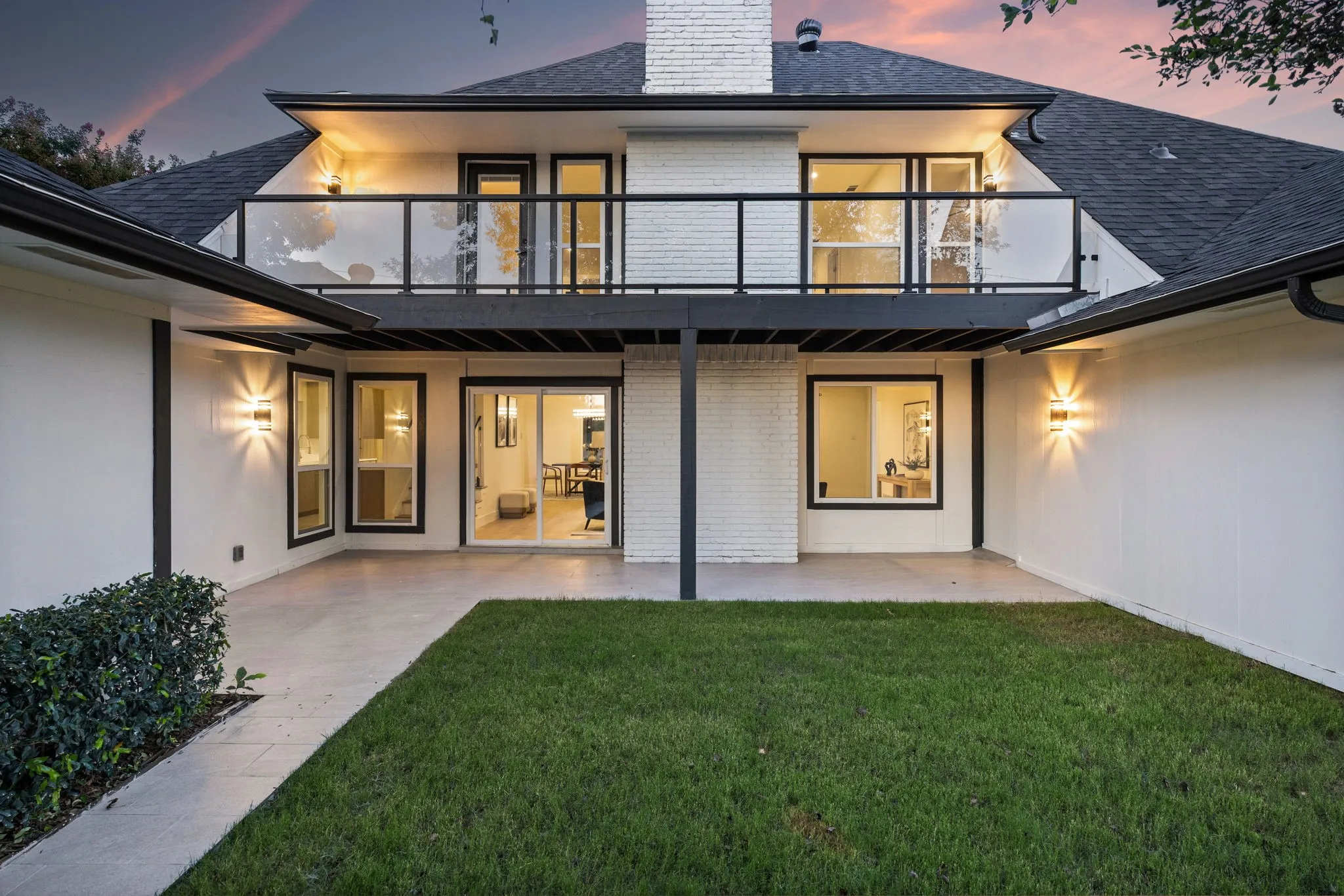Rear exterior featuring a ground-level patio, second-story balcony with a glass railing, and a grass lawn