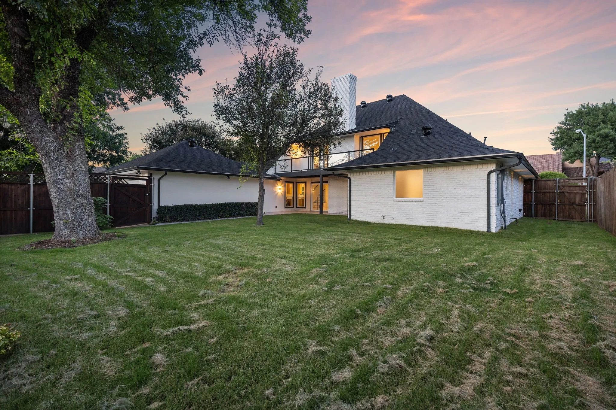 Expansive rear yard featuring a large mature tree, a privacy fence, and a white brick exterior with black trim