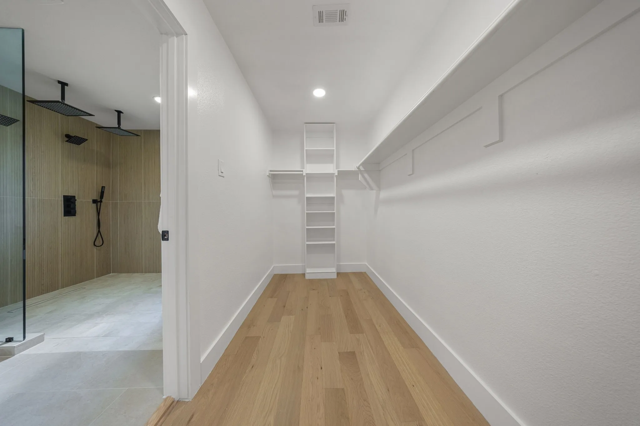 Spacious walk-in closet featuring wood-finish flooring, white built-in shelving, and white baseboards