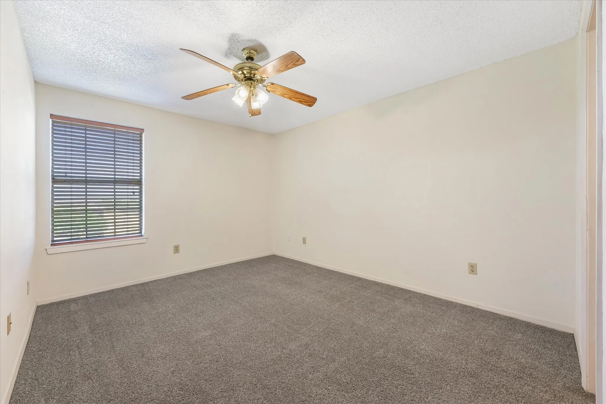 Room featuring soft gray carpeting, light neutral wall paint, and a wood-finish ceiling fan with integrated lighting