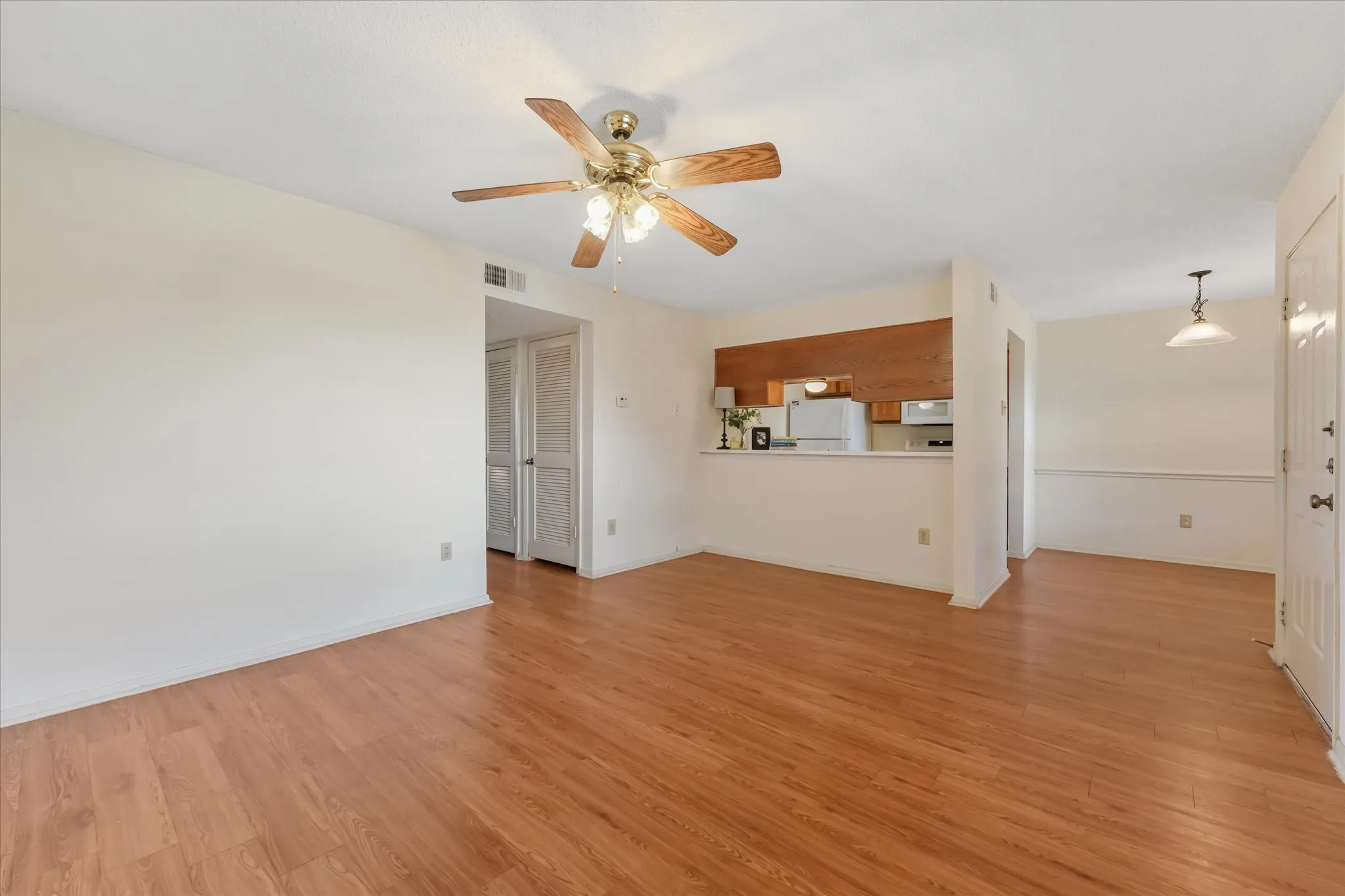 Spacious living area featuring wood-finish flooring, a ceiling fan with integrated lighting, and neutral wall tones