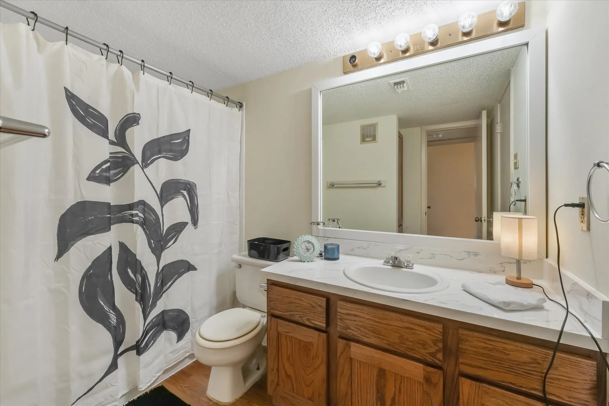 Bathroom featuring a wood-finish vanity with a white countertop and integrated sink, a large wall-mounted mirror, and overhead vanity lighting