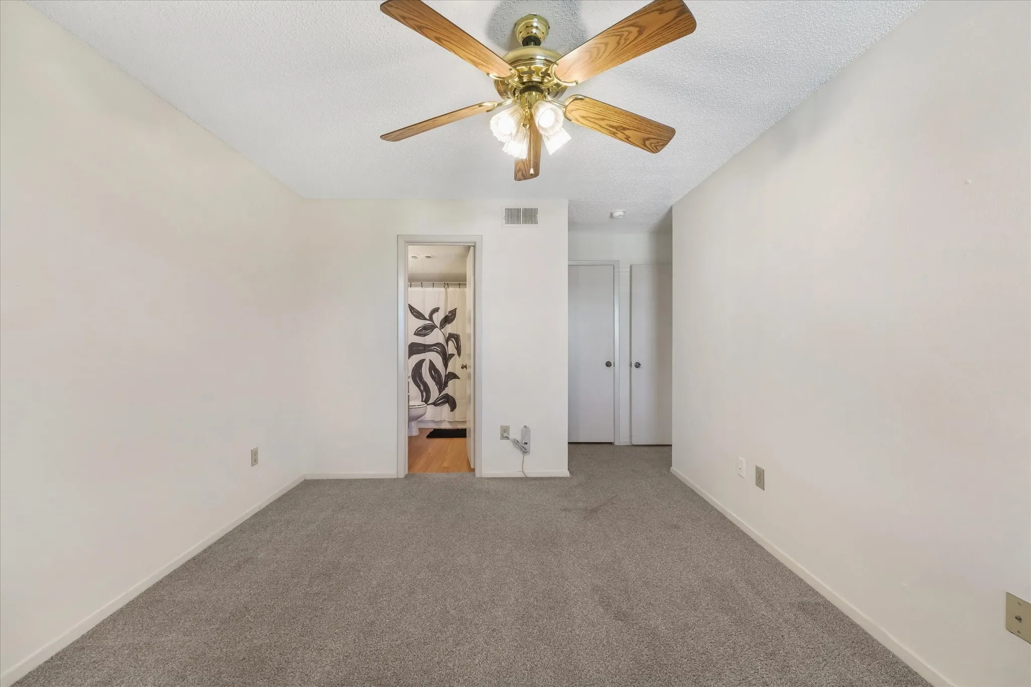 Carpeted room featuring a ceiling fan with wood-finish blades and brass-tone hardware