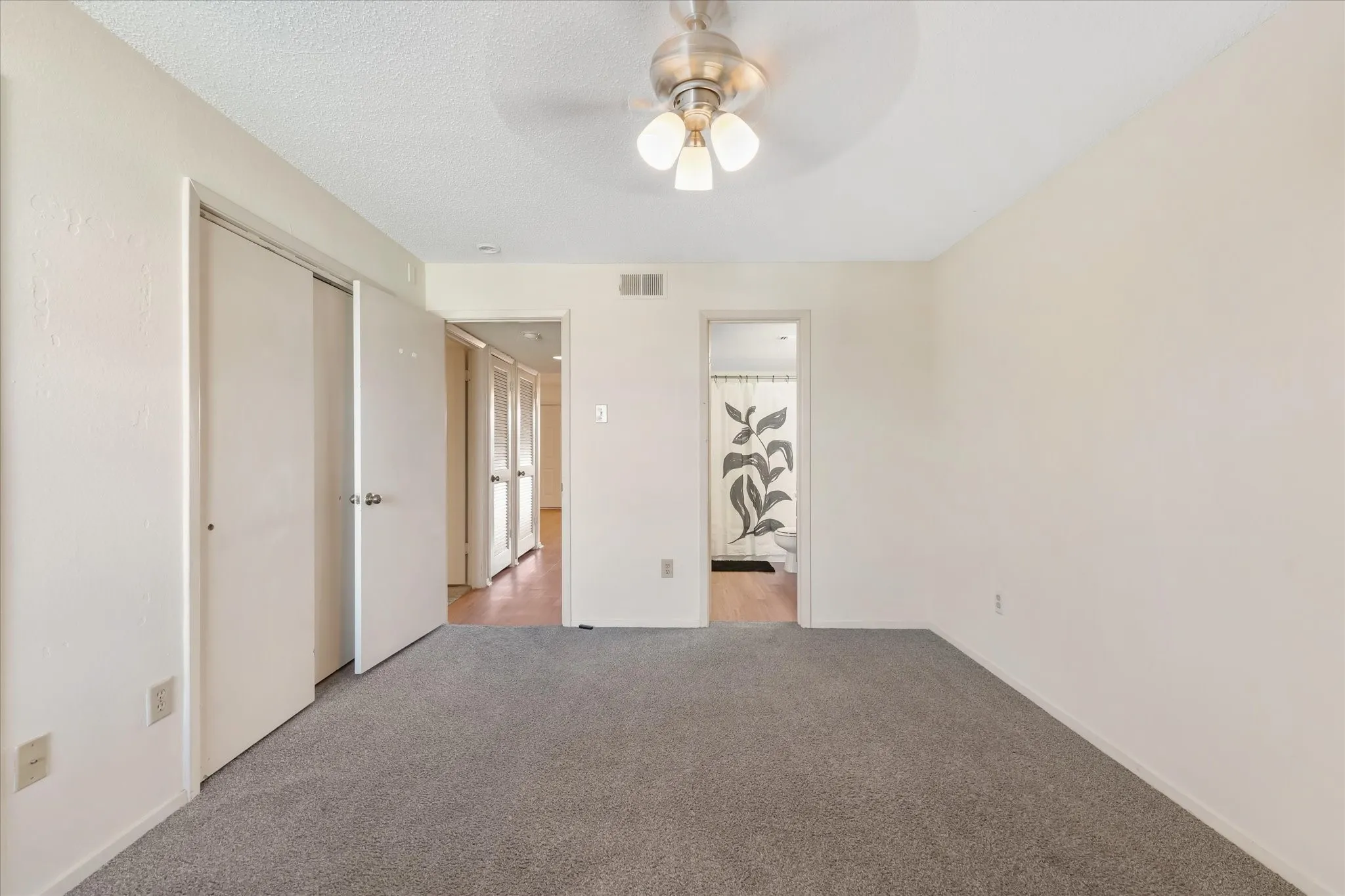 Carpeted room featuring a ceiling fan with integrated lighting, white walls, and two bi-fold closet doors
