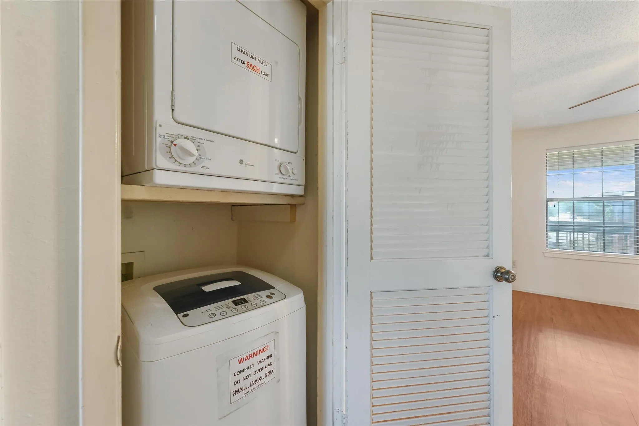 Dedicated laundry closet featuring a stackable washer and dryer unit, louvered bi-fold doors, and a wood-finish flooring visible in the background