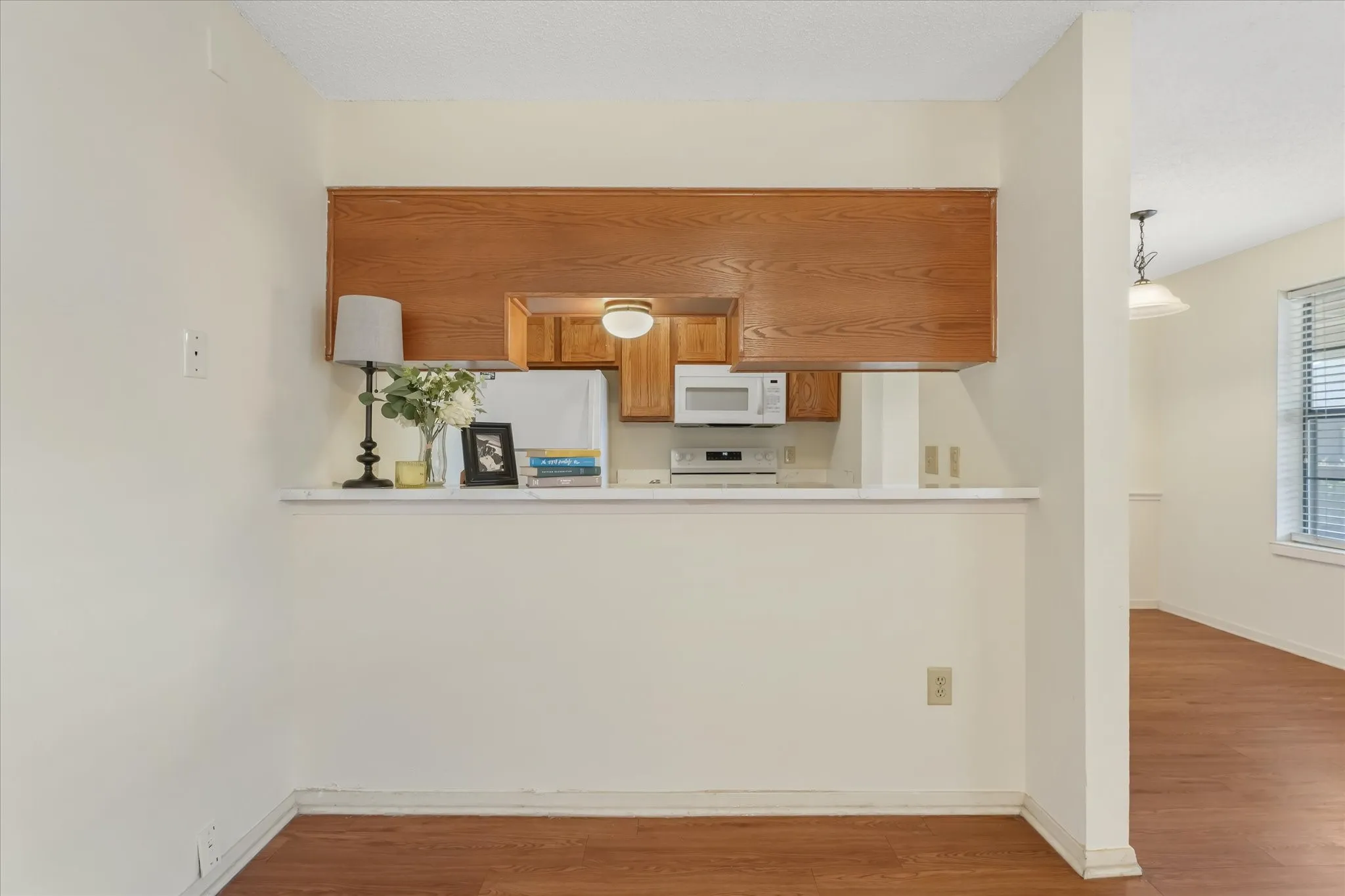 Kitchen pass-through with wood-finish upper cabinetry, a built-in microwave, and a white countertop