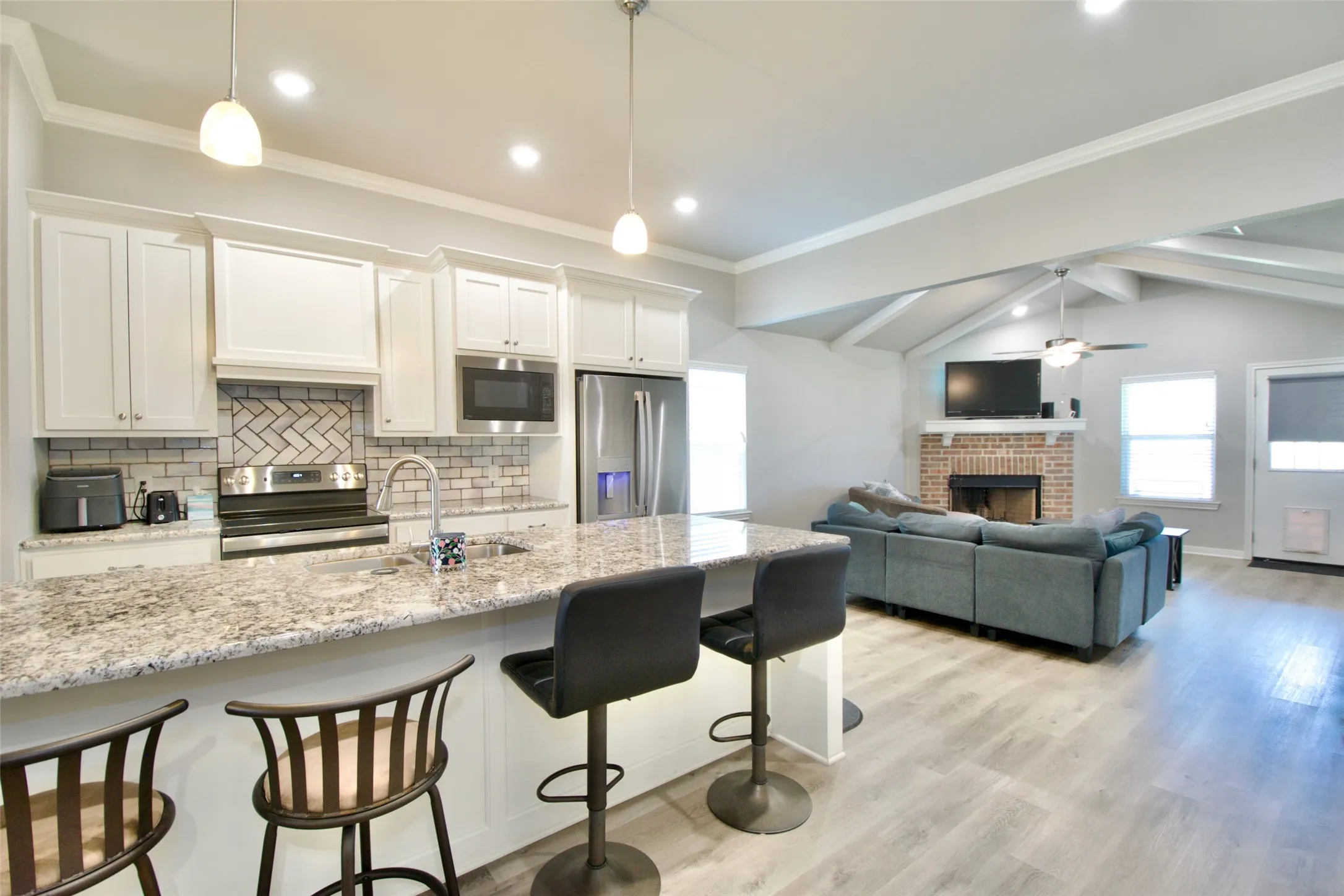 Open-concept living area featuring a kitchen with light-colored cabinetry, stainless steel appliances, and a granite-look island