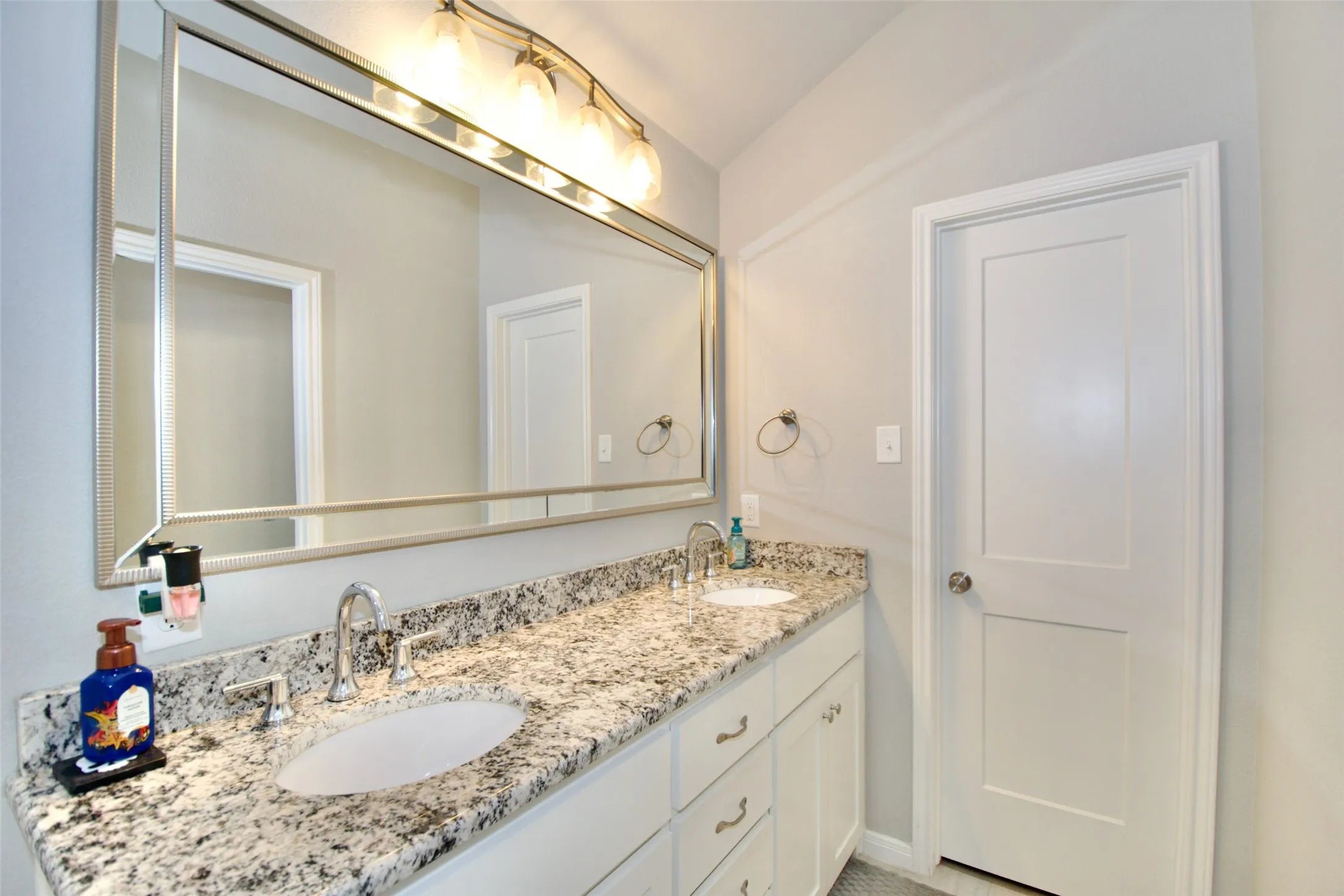 Double vanity featuring granite countertops with undermount sinks, chrome fixtures, white cabinetry, and a large framed mirror