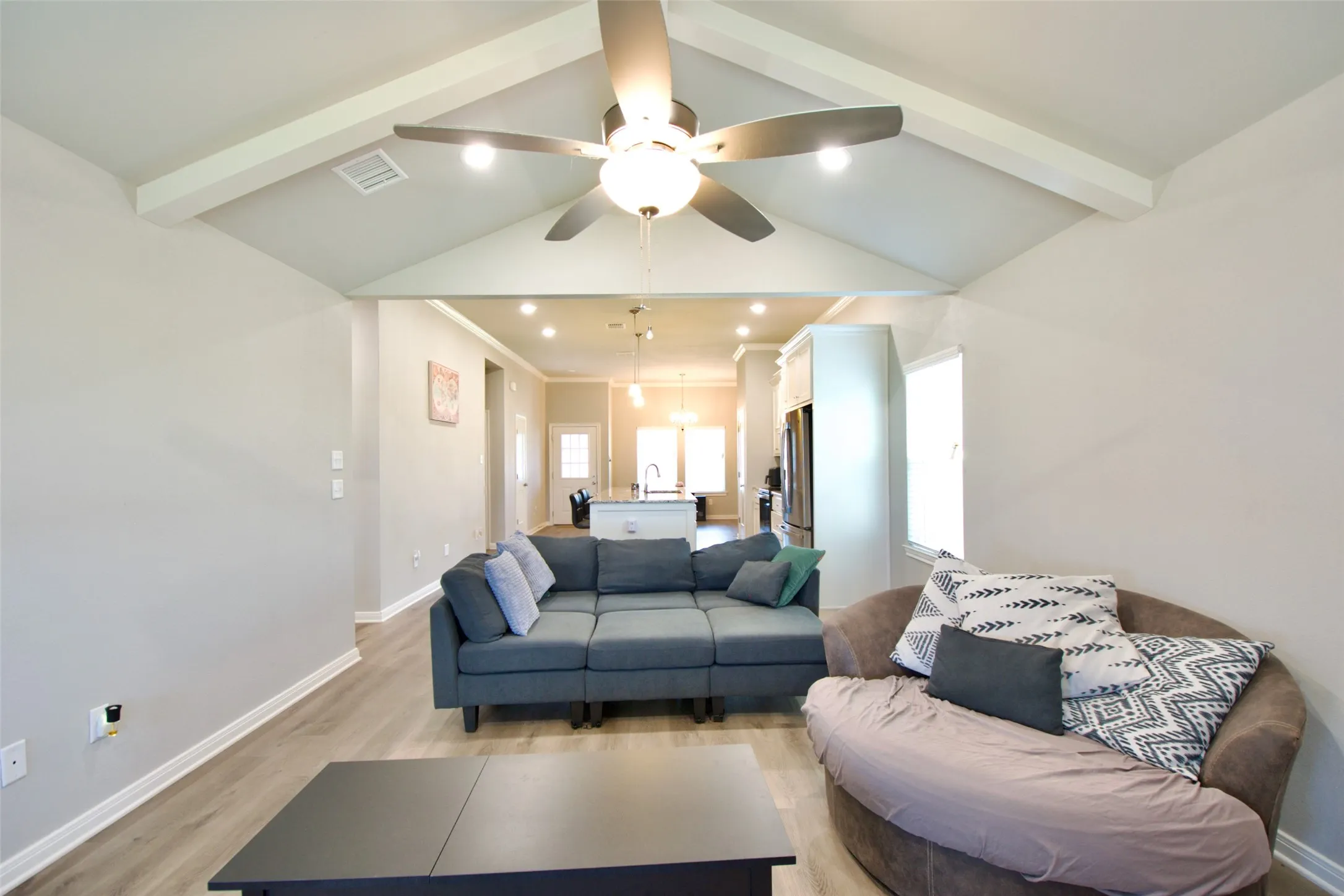Living area featuring vaulted ceilings with exposed beams, a ceiling fan with integrated lighting, recessed lighting, wood-finish flooring, and light gray wall paint
