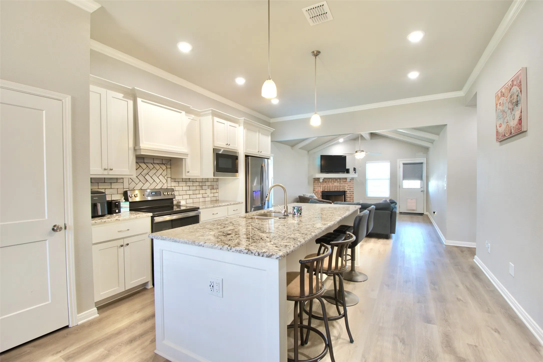 Well-appointed kitchen featuring white cabinetry, a herringbone tile backsplash, and a granite-finish island with seating