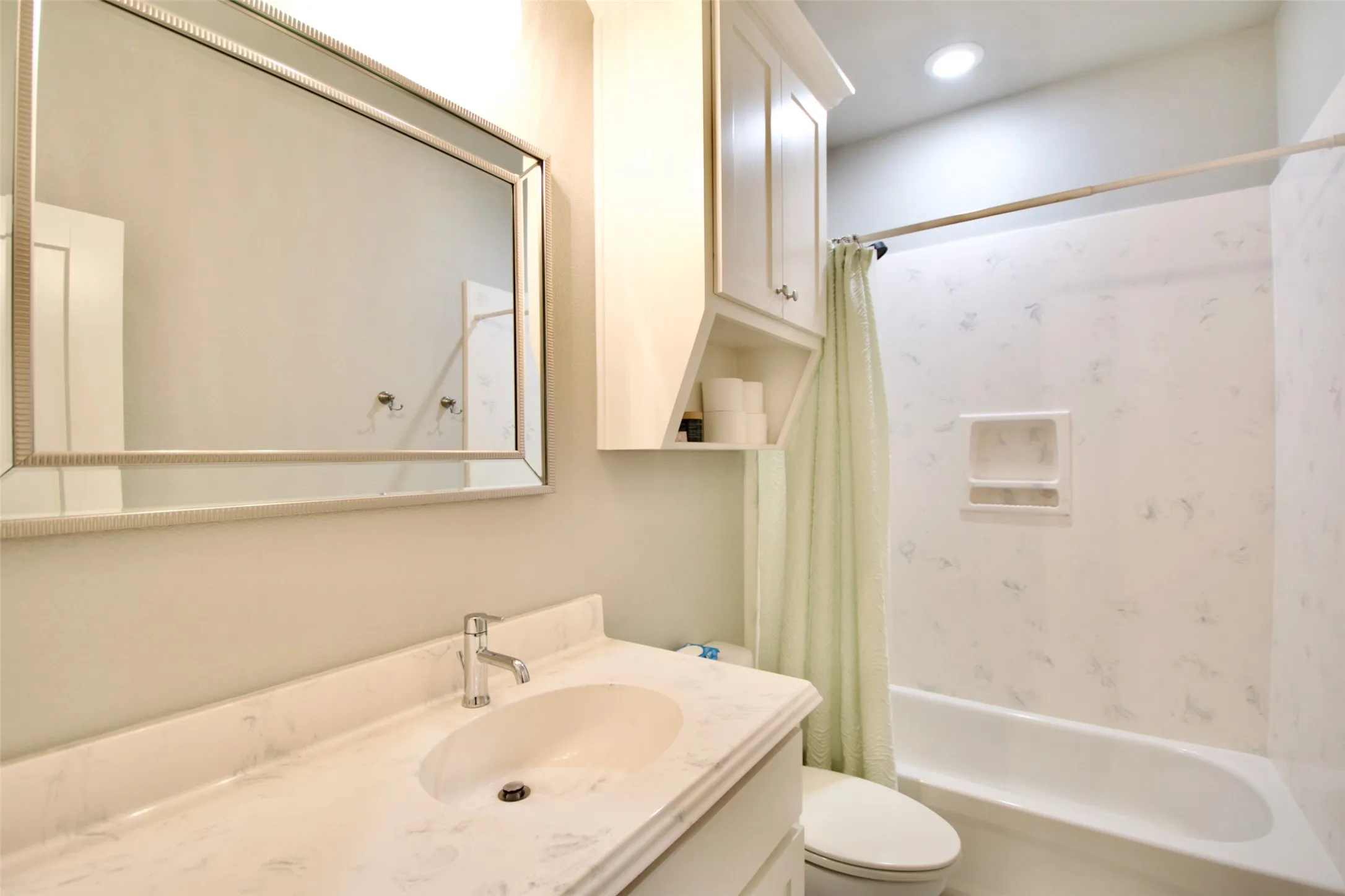Bathroom featuring a vanity with an integrated sink, a rectangular framed mirror, white cabinetry with open shelving, a built-in bathtub, and a shower with a patterned surround