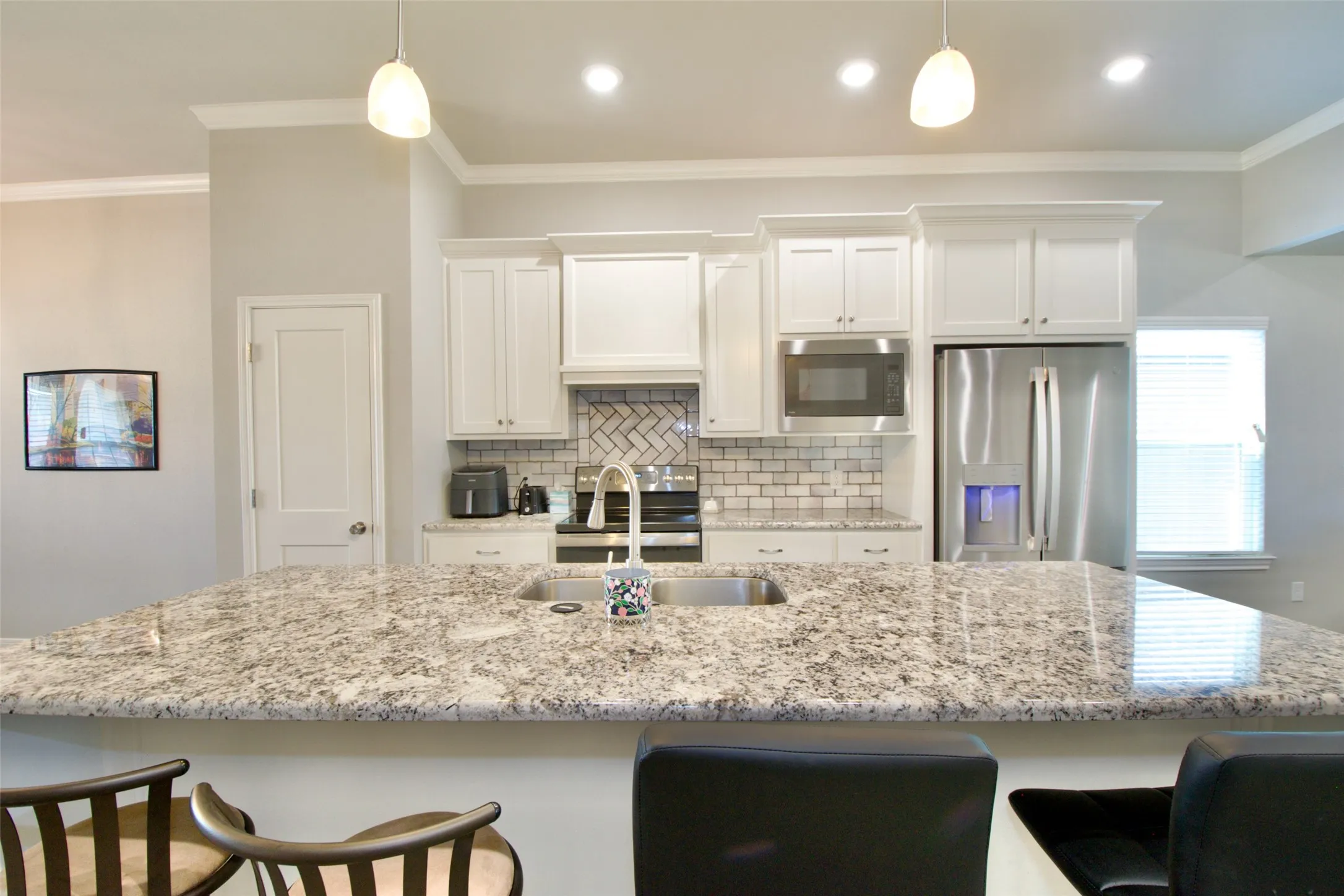 Kitchen featuring a large speckled countertop island with an undermount double basin sink and a high-arc faucet