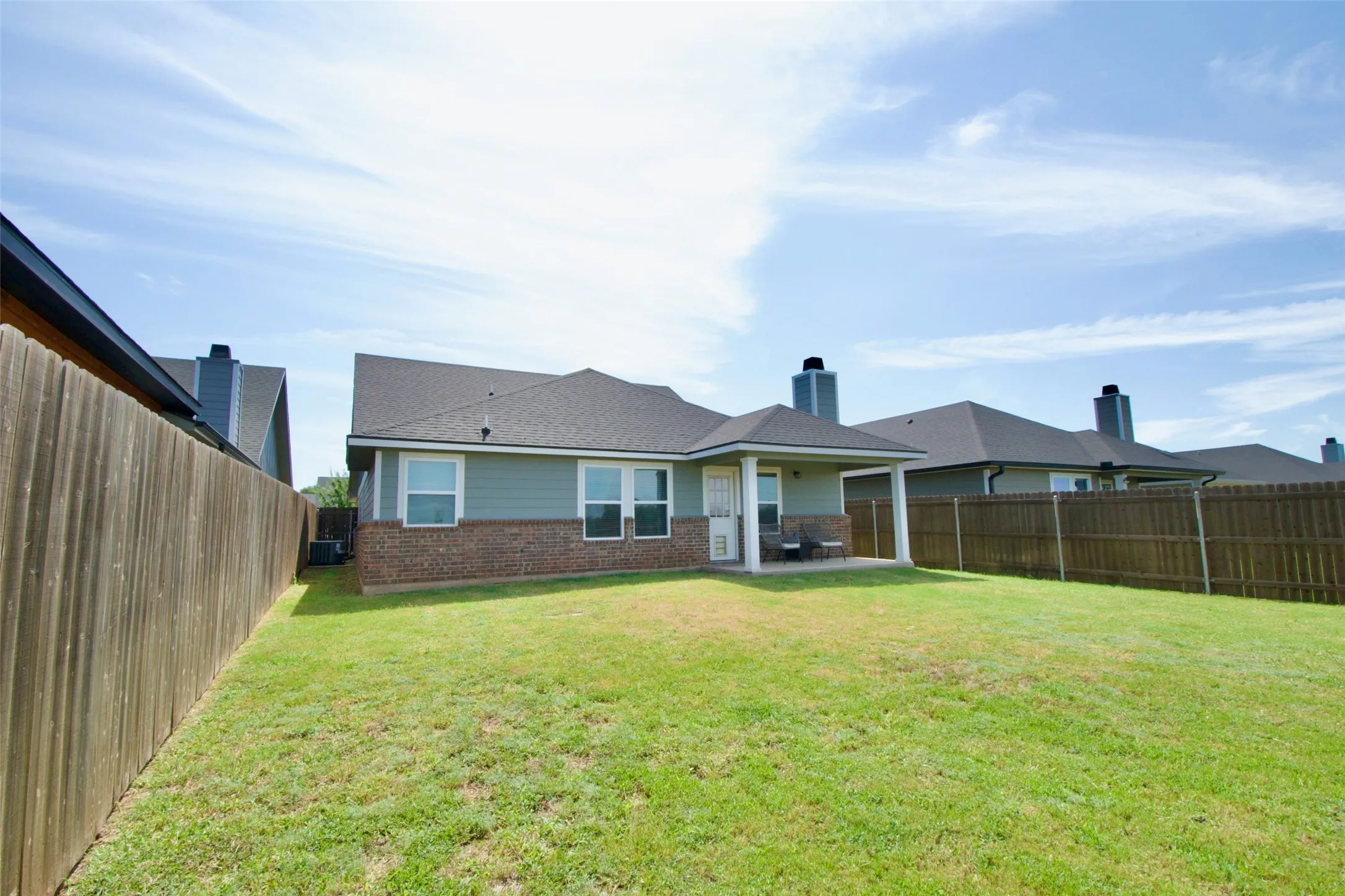 Expansive backyard with a covered patio, featuring a manicured lawn and privacy fencing
