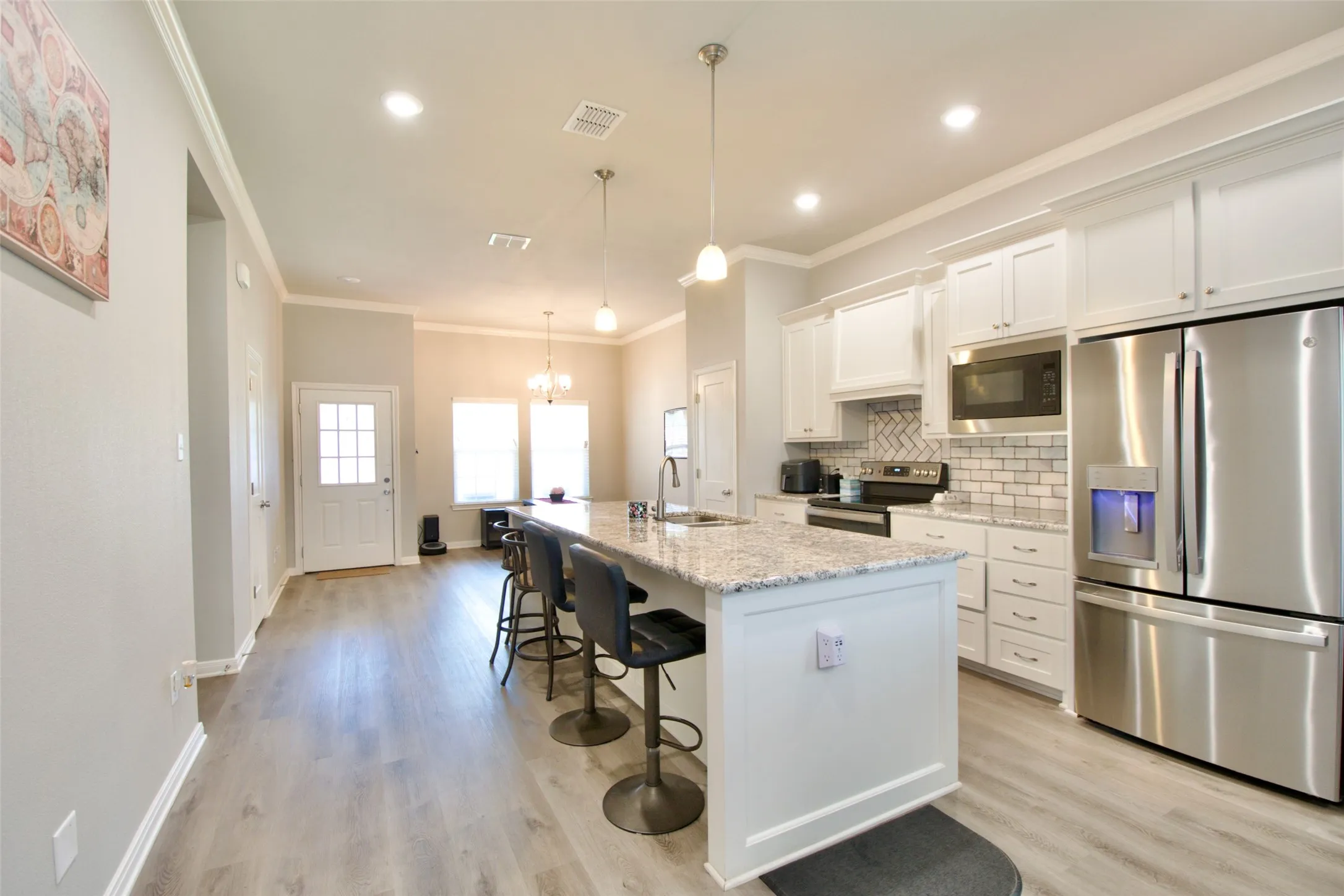 Open-concept kitchen featuring white cabinetry, granite countertops, a herringbone tile backsplash, stainless steel appliances, and wood-finish flooring