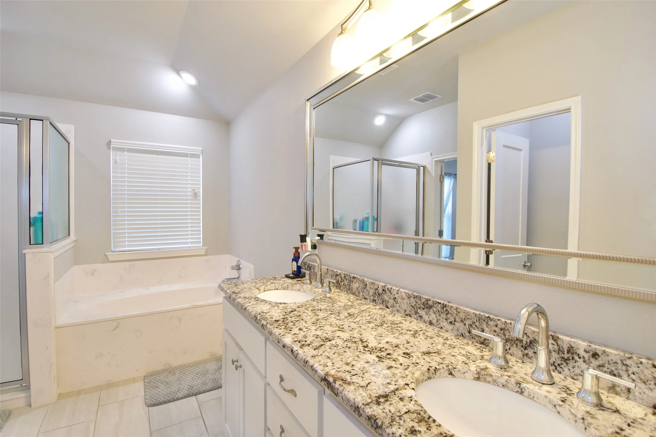 Bathroom featuring a dual vanity with granite-style countertops, an integrated soaking tub, a separate glass-enclosed shower, and tile flooring
