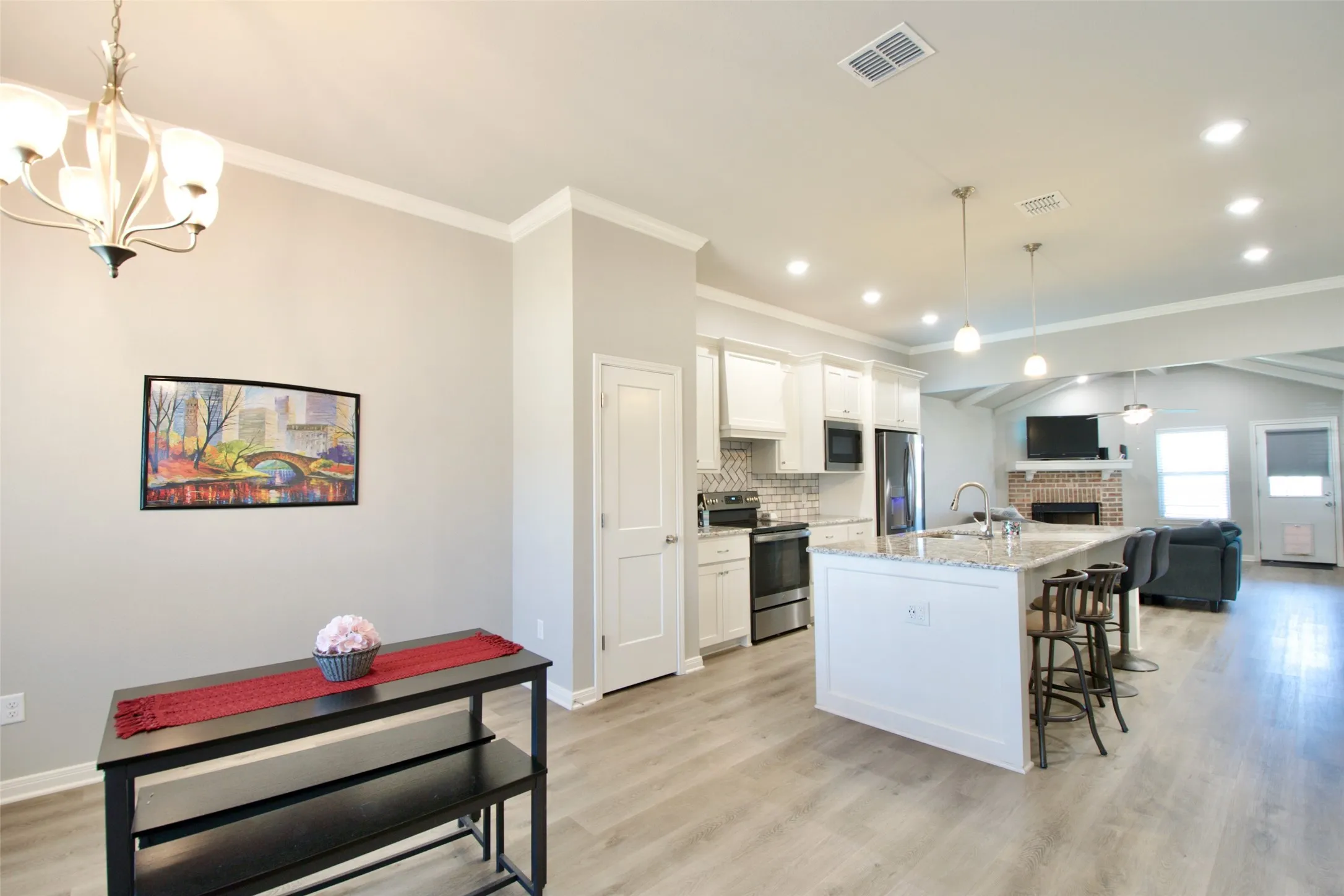 Open-concept living area featuring a kitchen island with granite-finish countertop, stainless steel appliances, wood-finish flooring, recessed lighting, and a brick fireplace