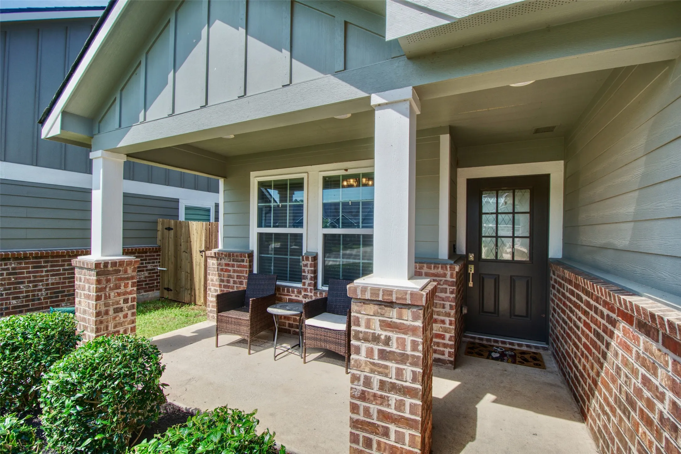 Inviting front porch featuring brick columns and wainscoting, a dark entry door with decorative glass, and siding exterior