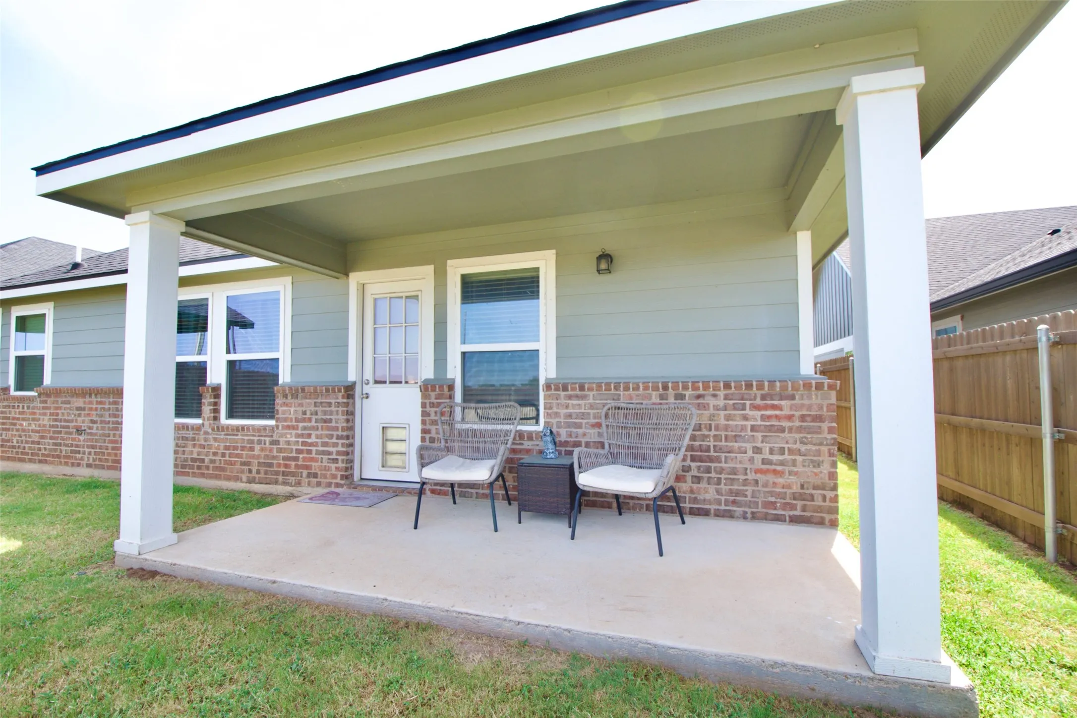 Covered concrete patio featuring white support columns and a light green exterior with brick skirting