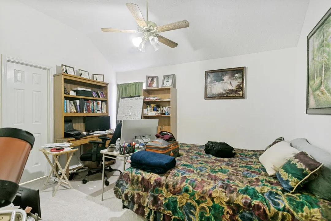 Vaulted ceiling with a ceiling fan light fixture, white walls, and light-colored carpeting