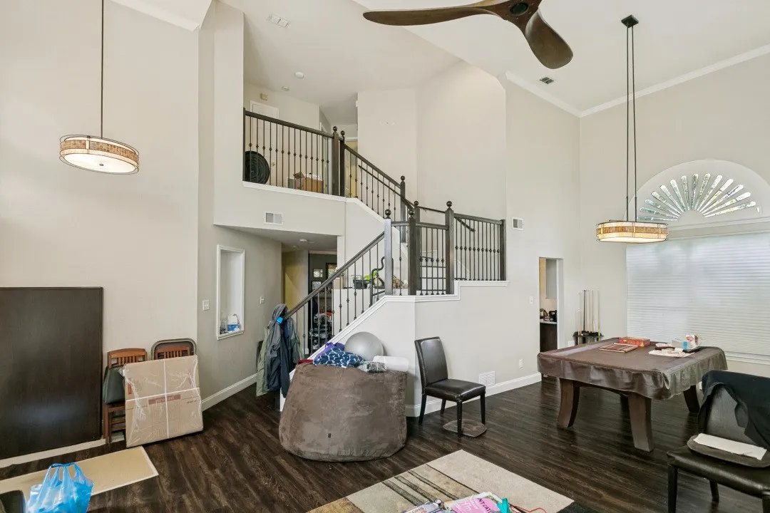 Two-story living area featuring wood-finish flooring, a grand staircase with dark iron balusters, high ceilings, and crown molding