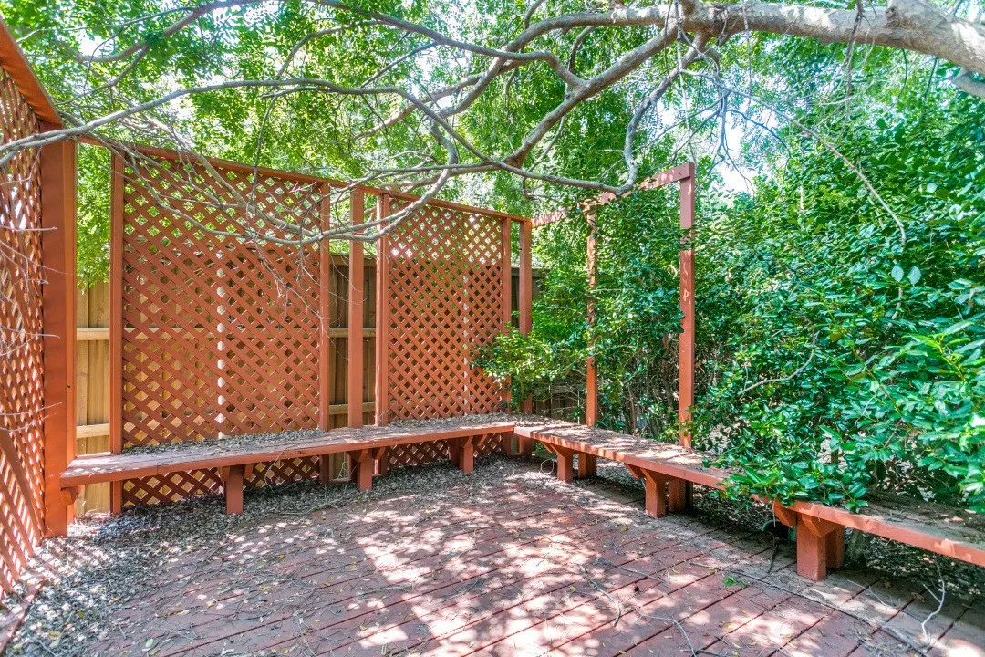 Private outdoor area featuring a brick patio, built-in wood benches, decorative lattice screens, and mature foliage
