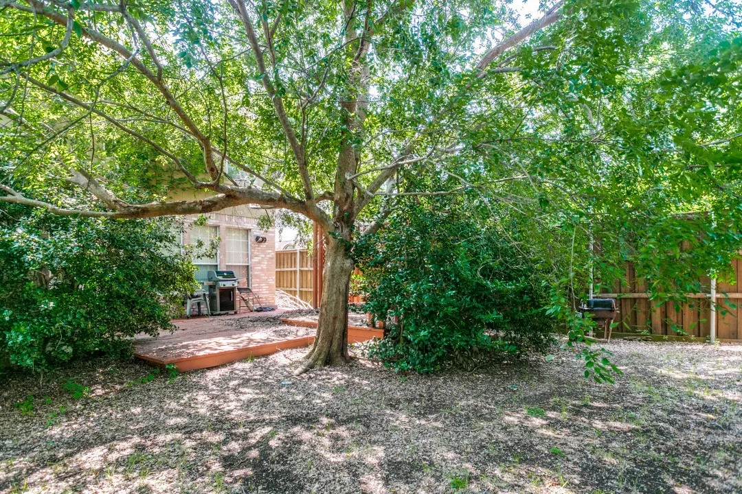 Secluded backyard featuring a mature shade tree, a wooden deck, a privacy fence, and brick exterior