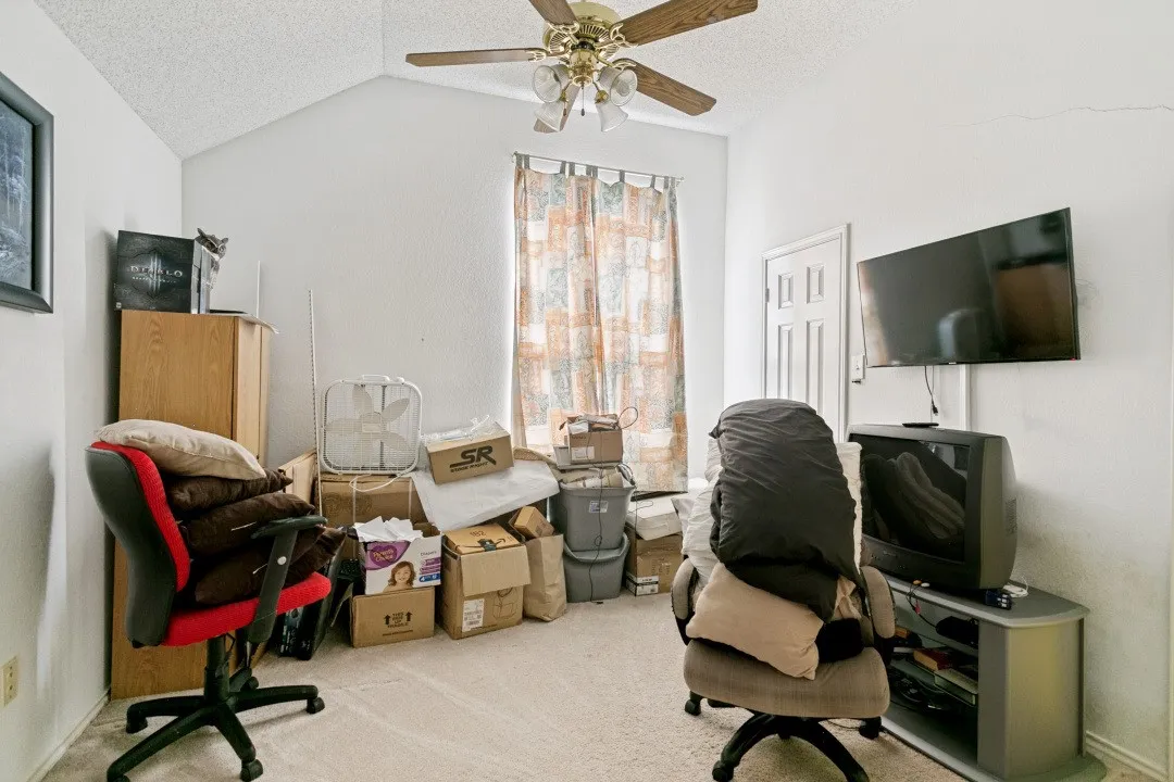 Room featuring a vaulted ceiling with a ceiling fan, wall-to-wall carpeting, and a window with patterned curtains